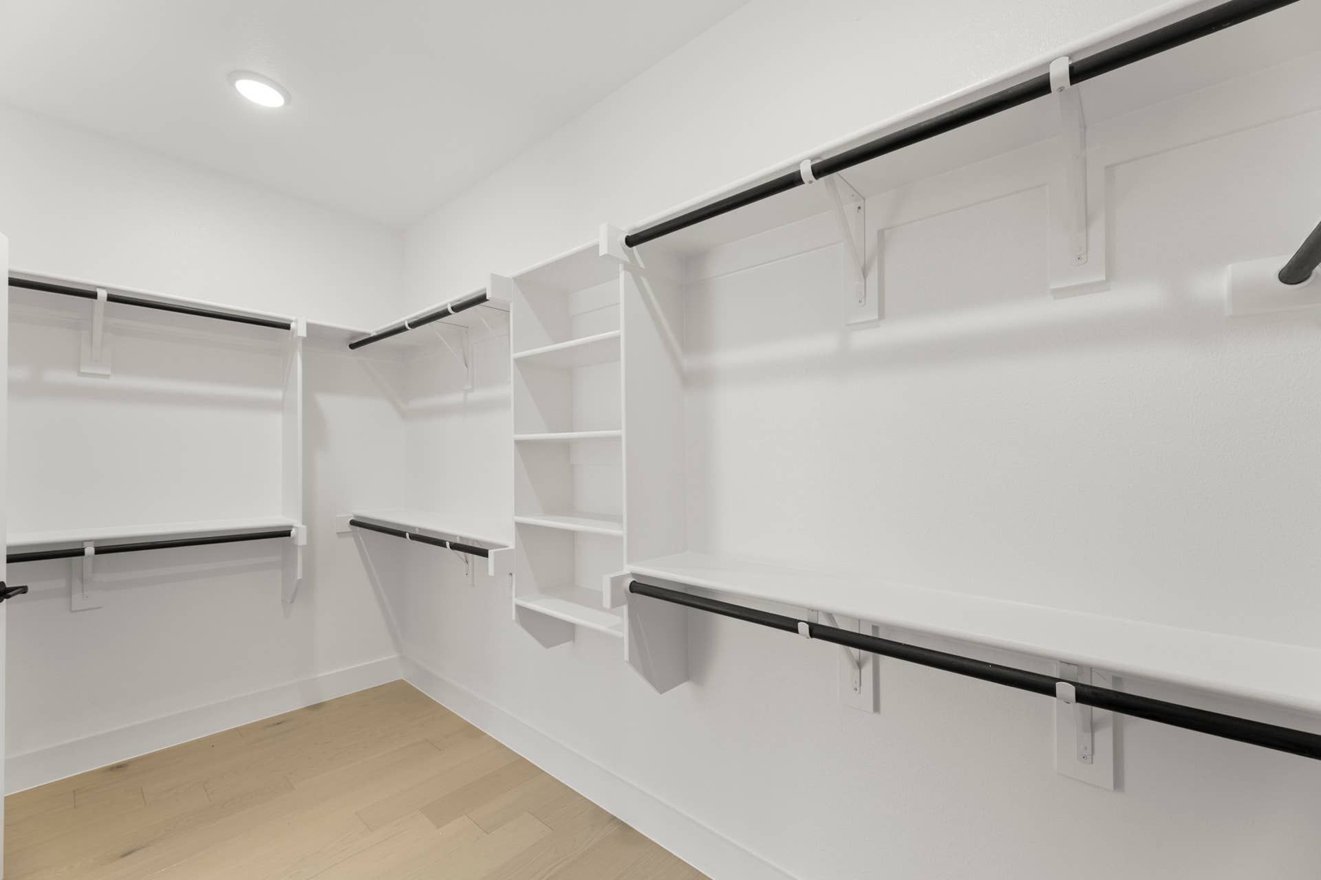 Spacious walk-in closet with white shelving and hanging rods.