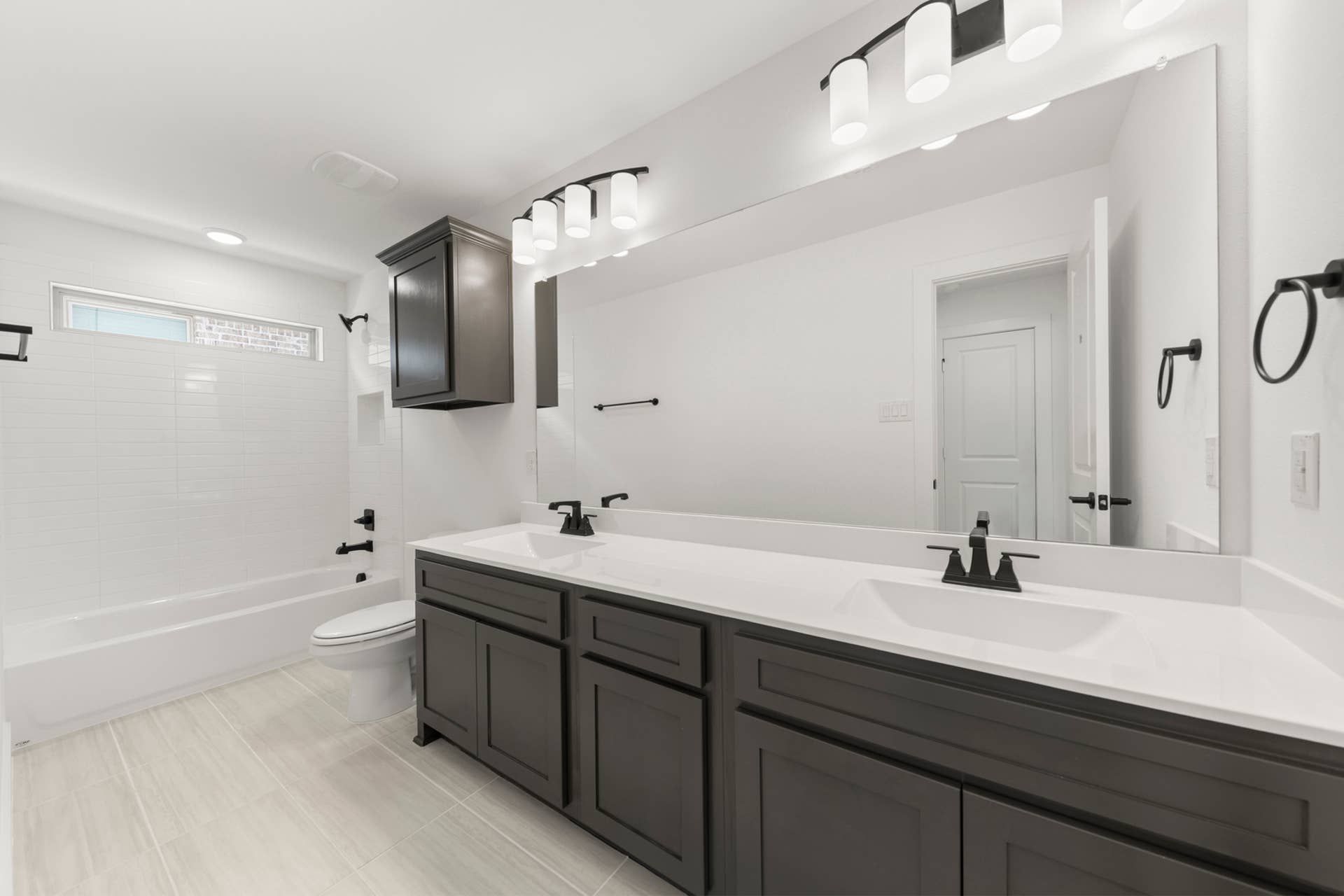 Modern bathroom with dual sinks, dark cabinetry, and bright lighting.