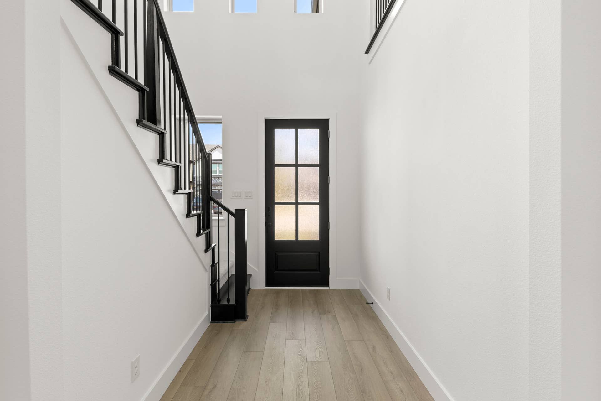 Bright entryway with black door, staircase, and light wood flooring.