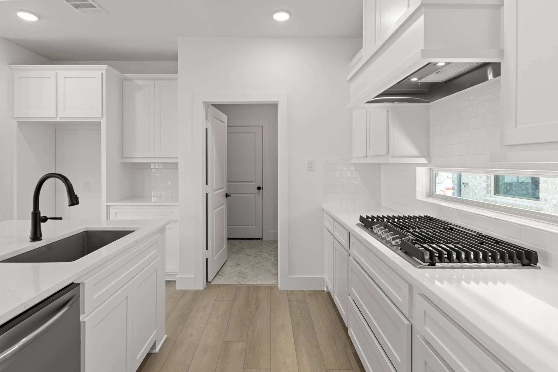Modern kitchen with white cabinetry, wood flooring, and sleek black faucet.