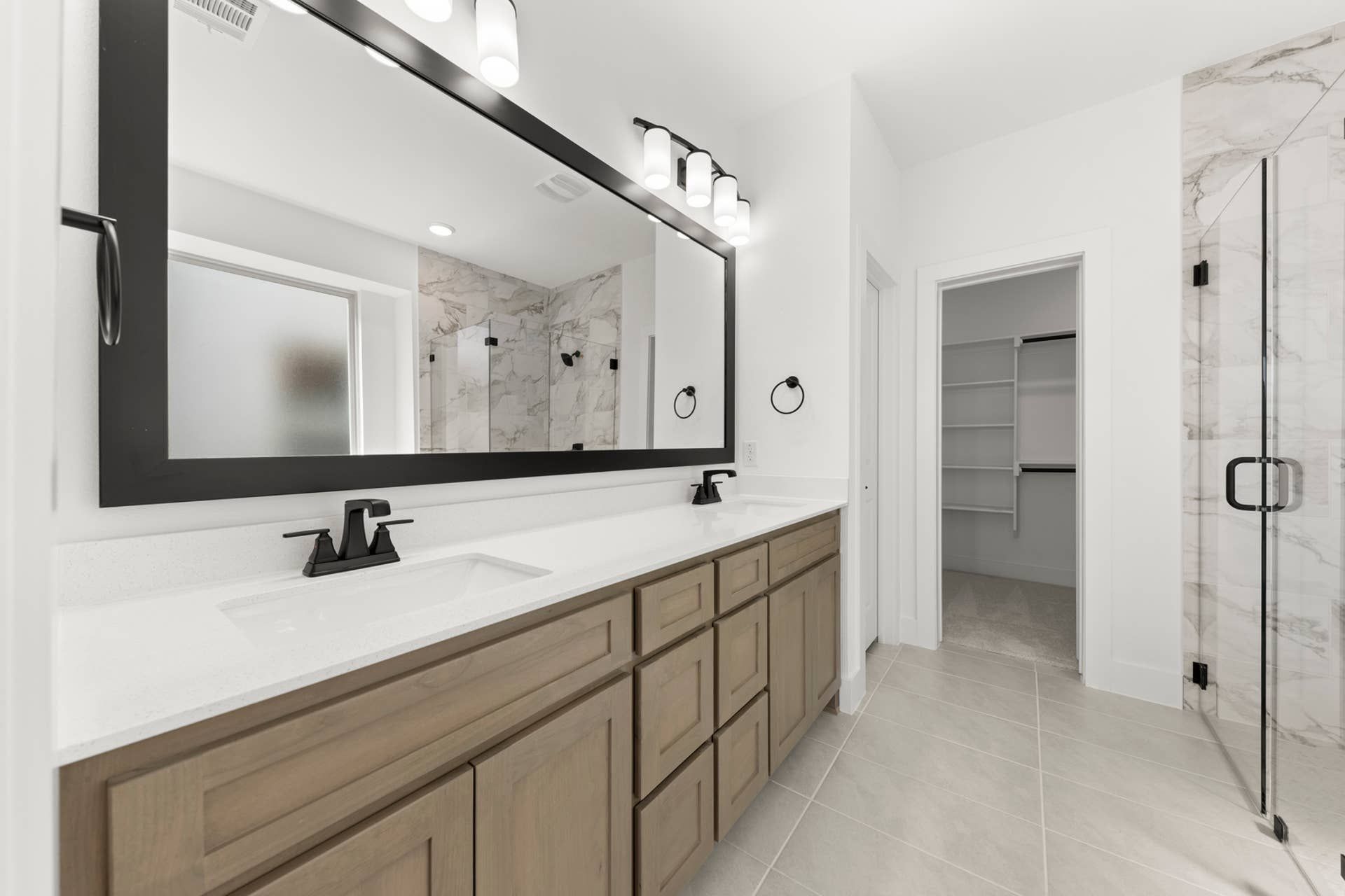 Modern bathroom with dual sinks, large mirror, and marble shower.