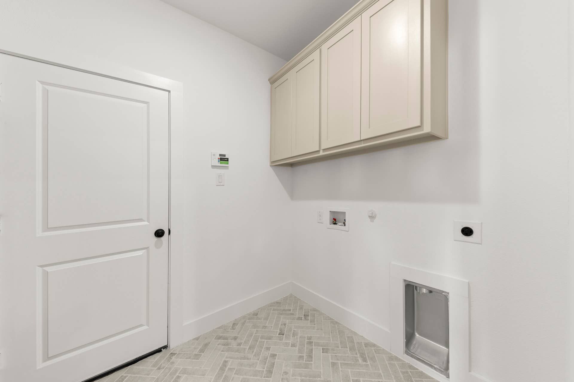 Utility room with herringbone tile flooring and overhead cabinetry.