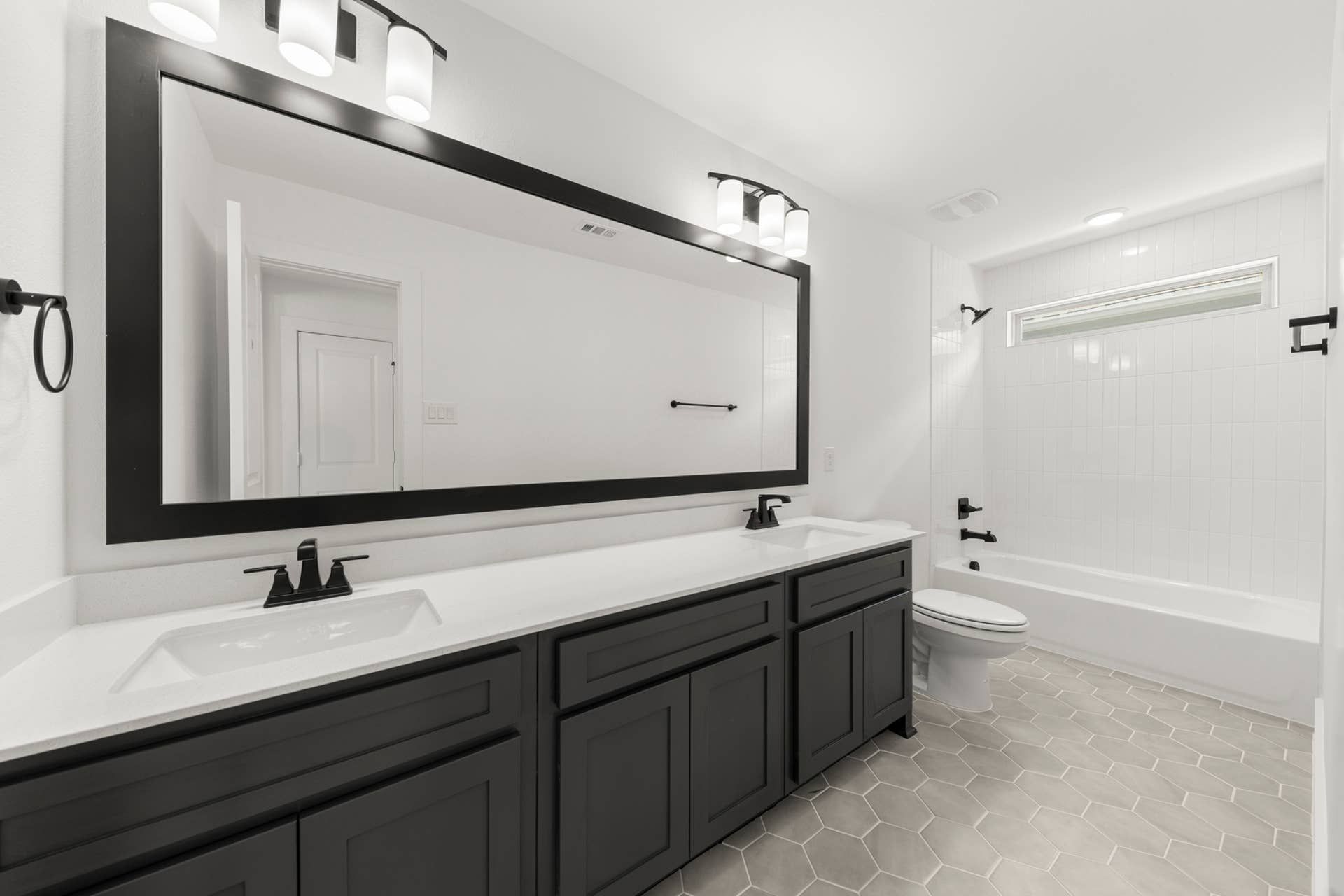 Modern bathroom with dual sinks, large mirror, and hexagonal tile flooring.