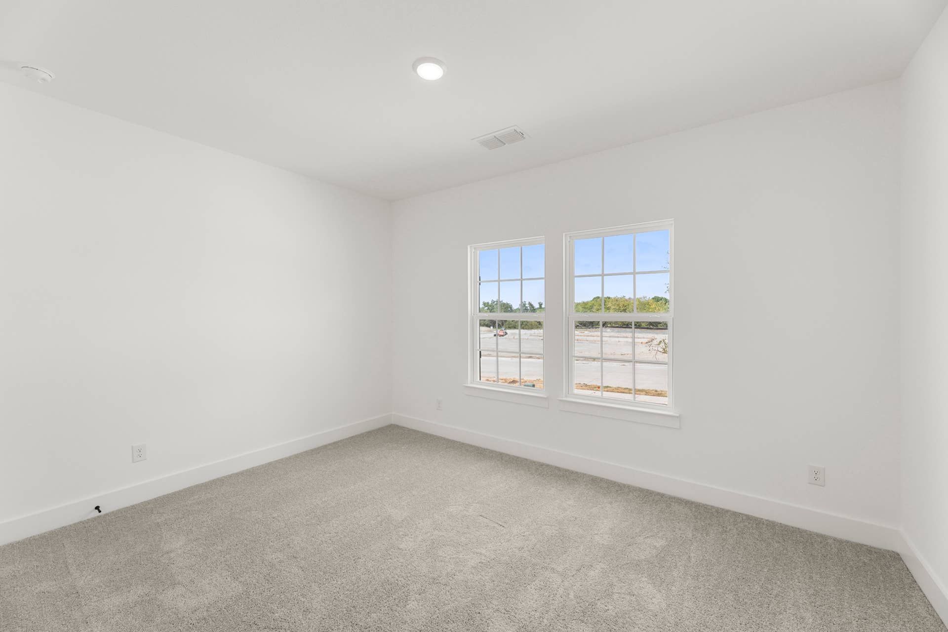 Spacious bedroom interior with carpet flooring and large double windows.