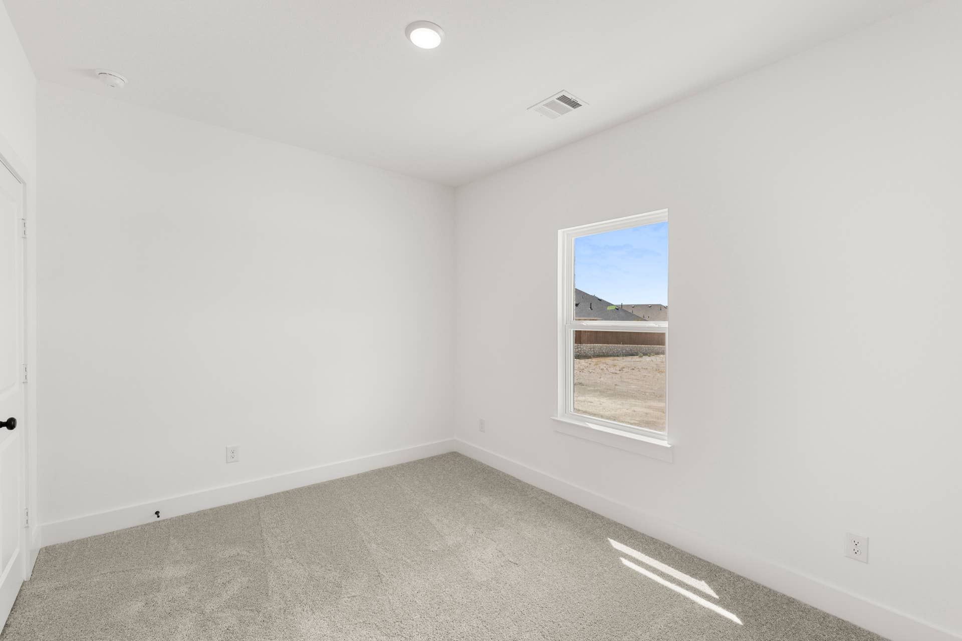 Bright empty bedroom with carpet flooring and a single window.