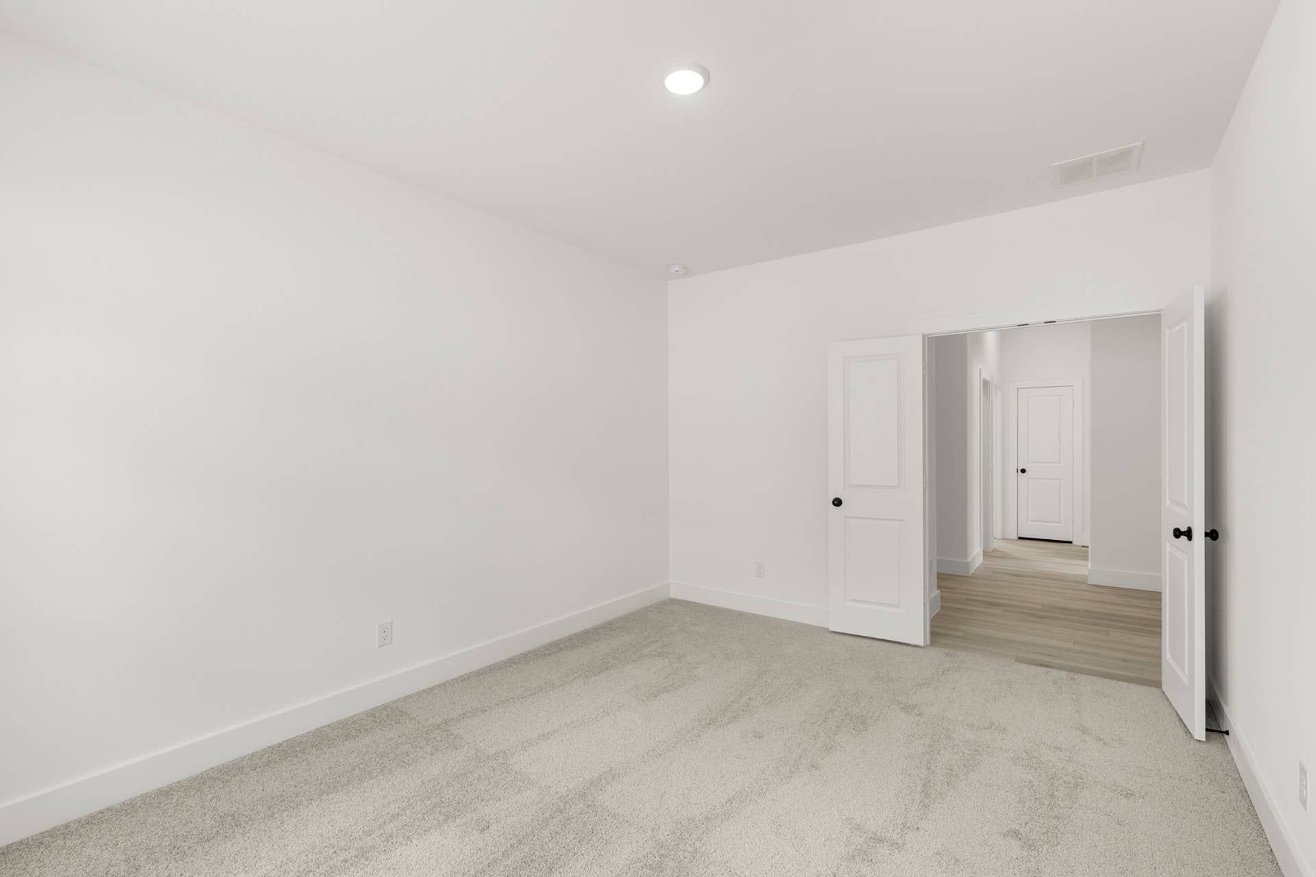 Minimalist study room with carpet and white walls, featuring open double doors.
