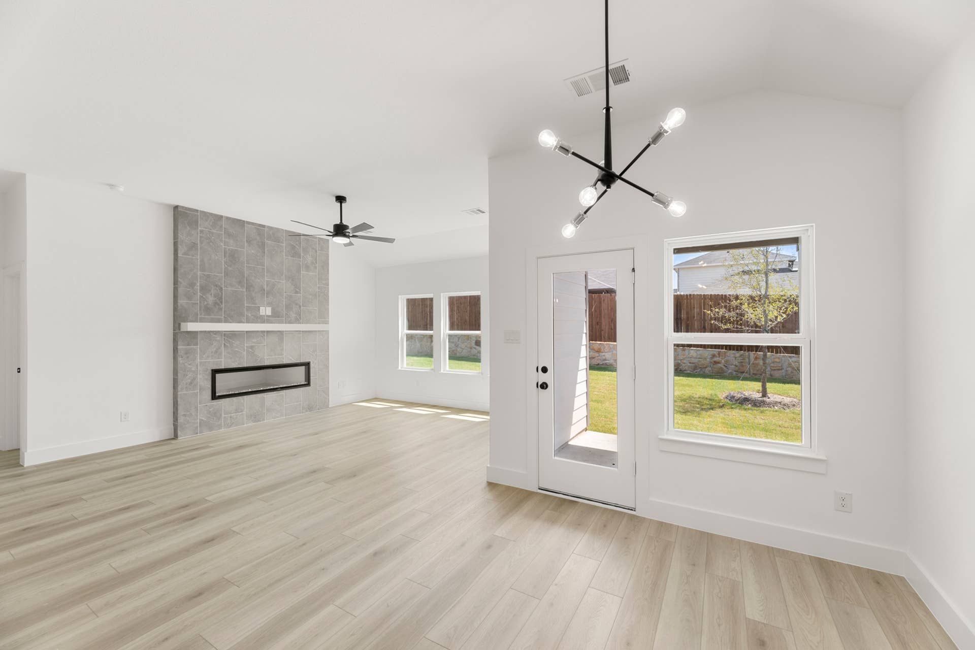 Spacious living room with modern chandelier, fireplace, and large windows overlooking backyard.