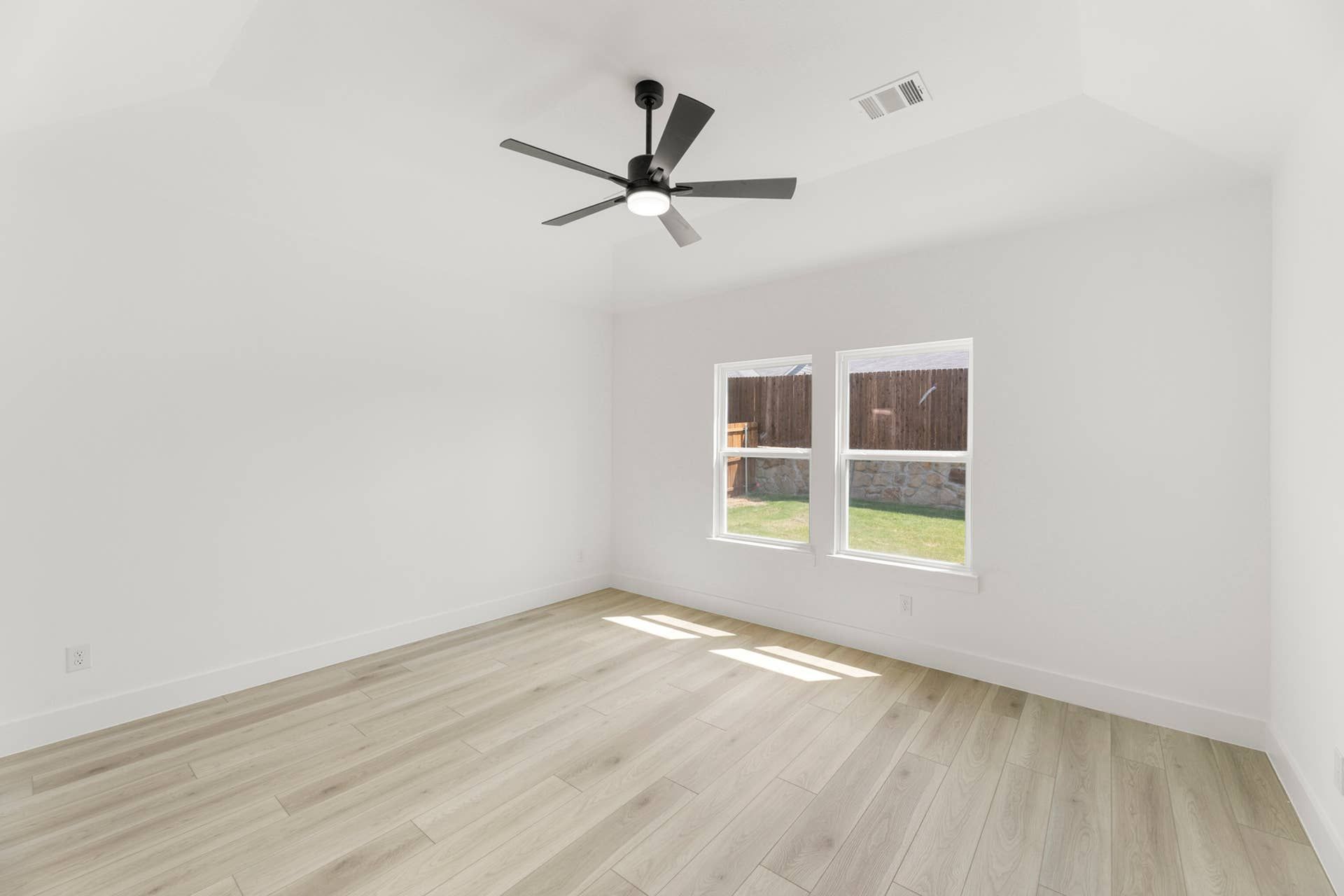 Bright empty room with hardwood floors and ceiling fan.