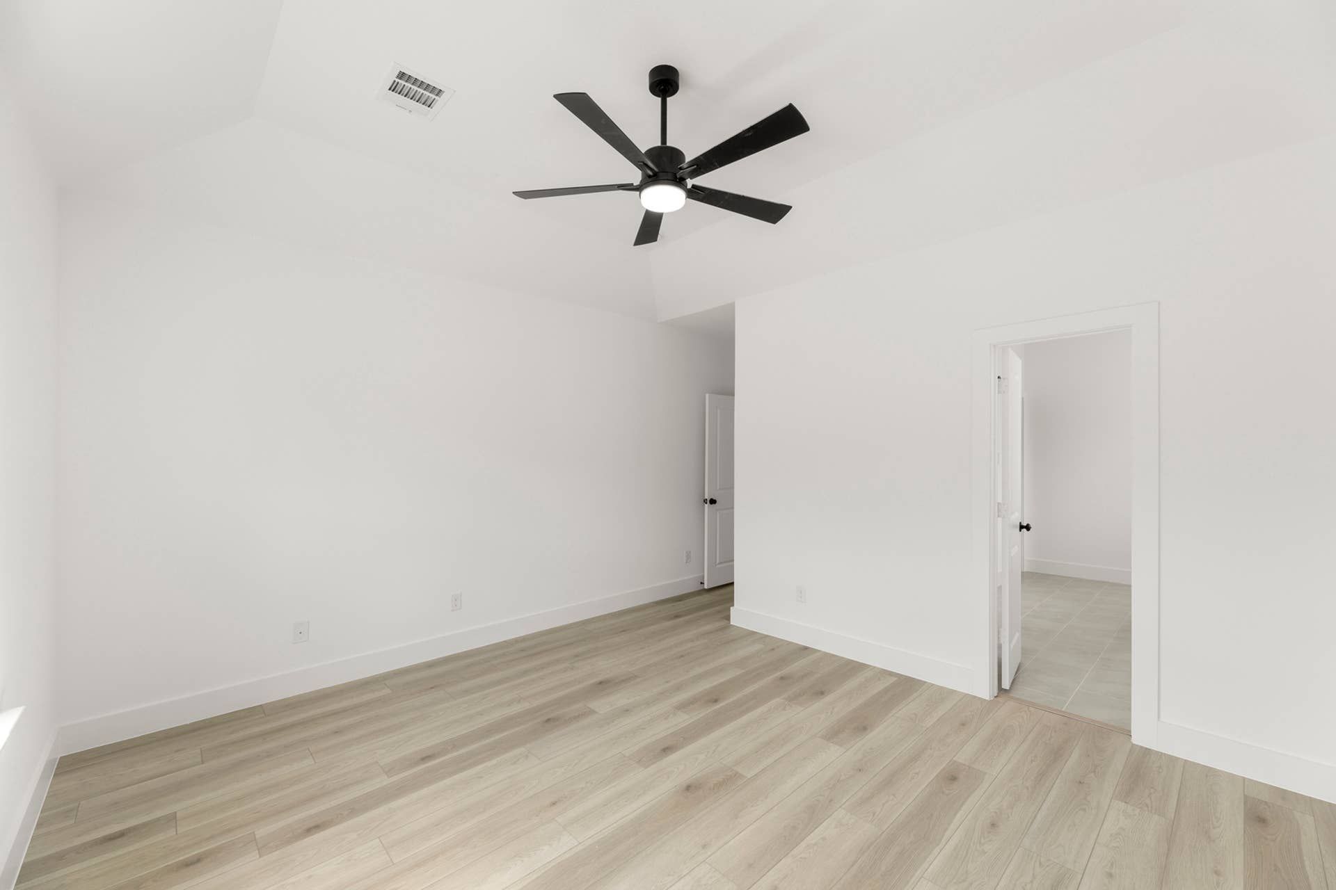 Spacious interior room with wood flooring and modern ceiling fan.