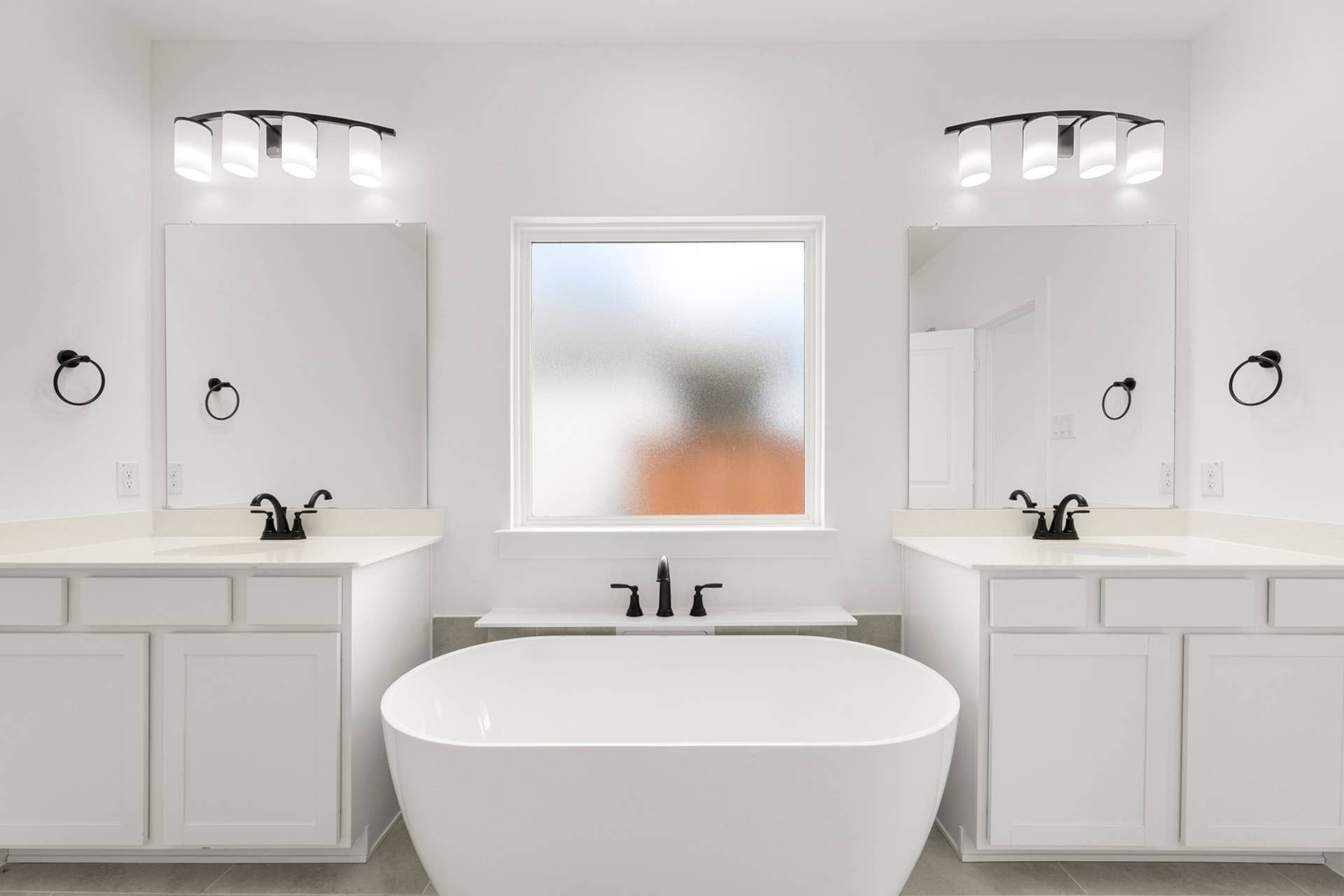 Modern bathroom with dual vanities, freestanding tub, and frosted window.