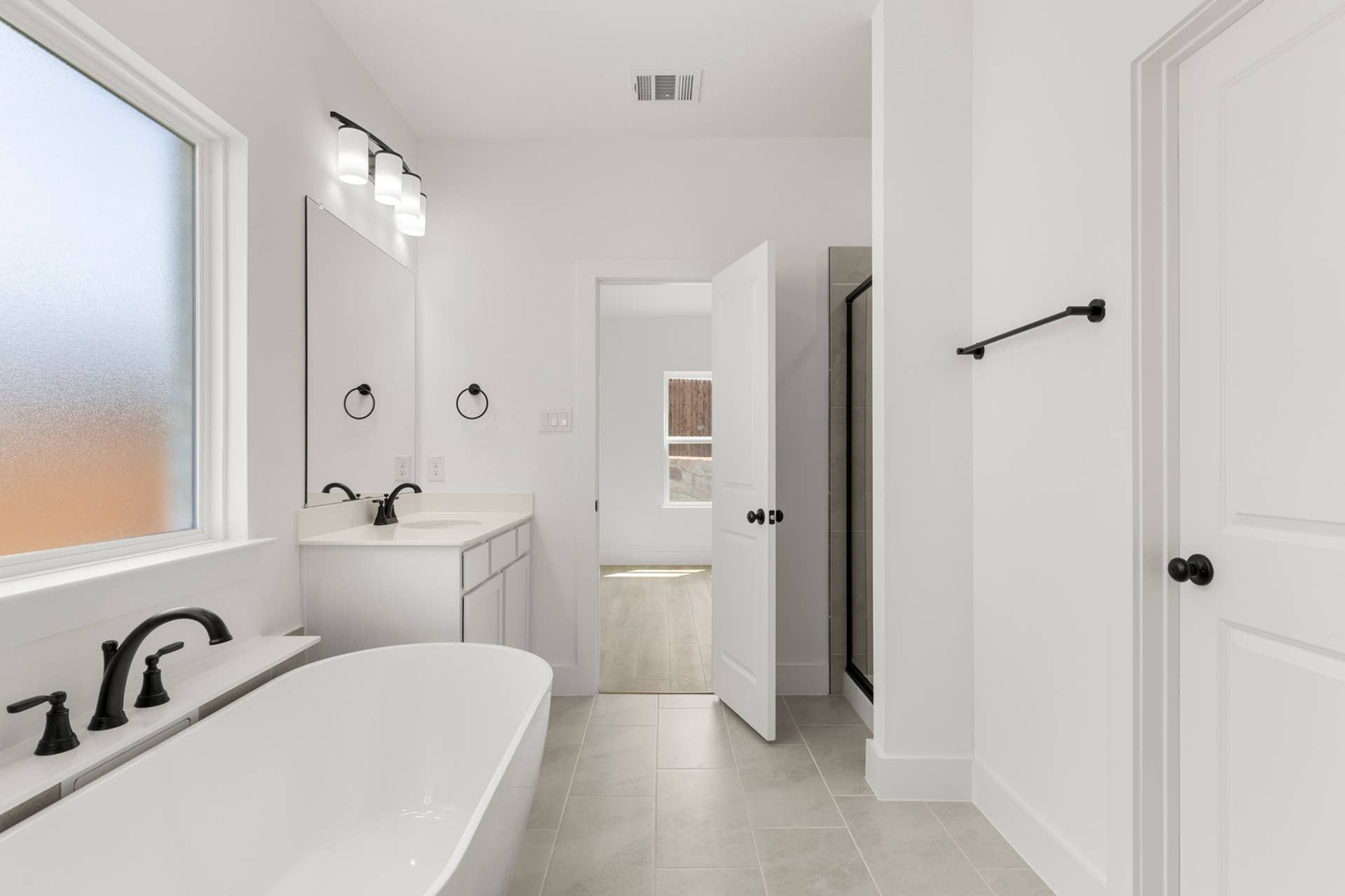 Modern bathroom with freestanding tub, white vanity, and frosted window.