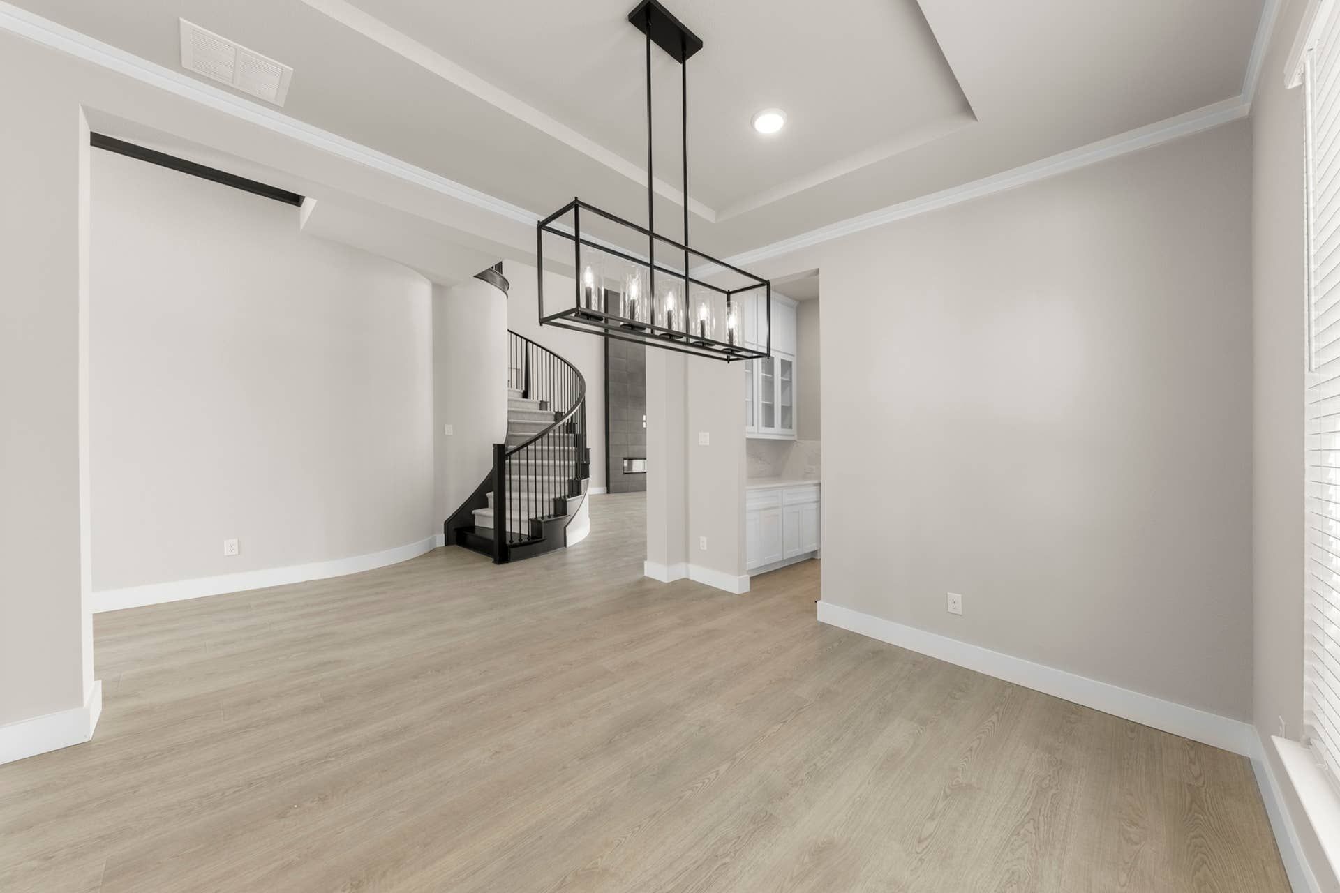 Modern dining room with spiral staircase and elegant chandelier lighting.