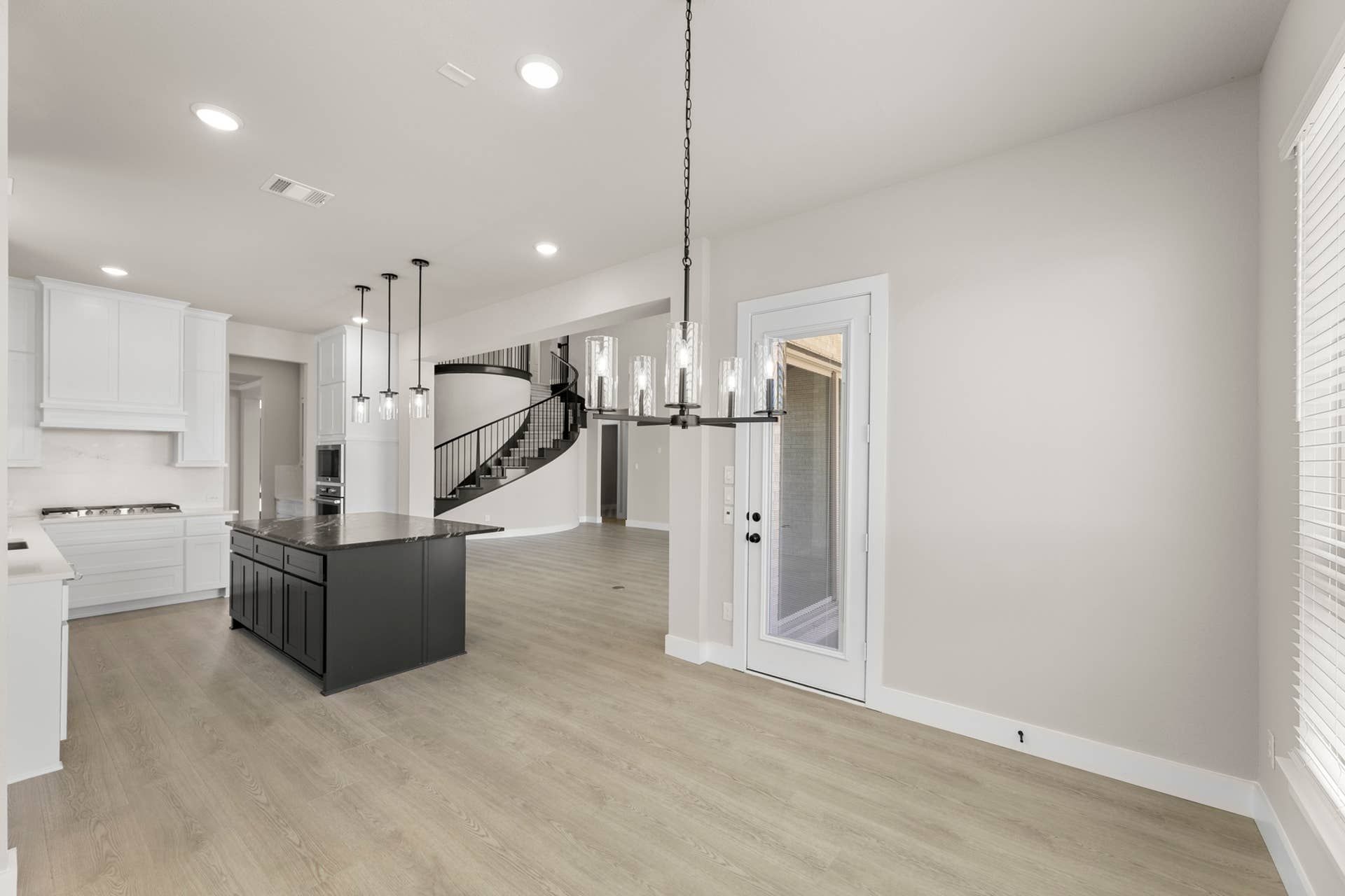 Spacious kitchen nook with modern island, pendant lighting, and spiral staircase view.