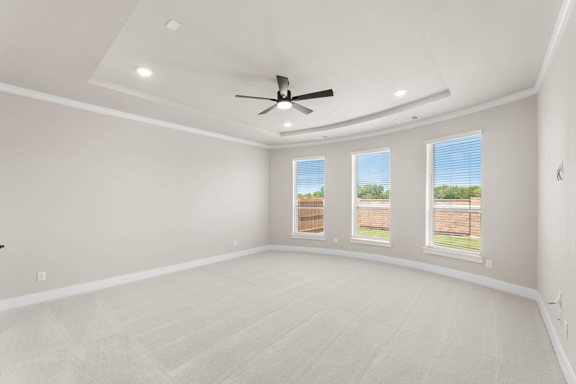 Spacious interior room with tray ceiling, ceiling fan, and large windows.