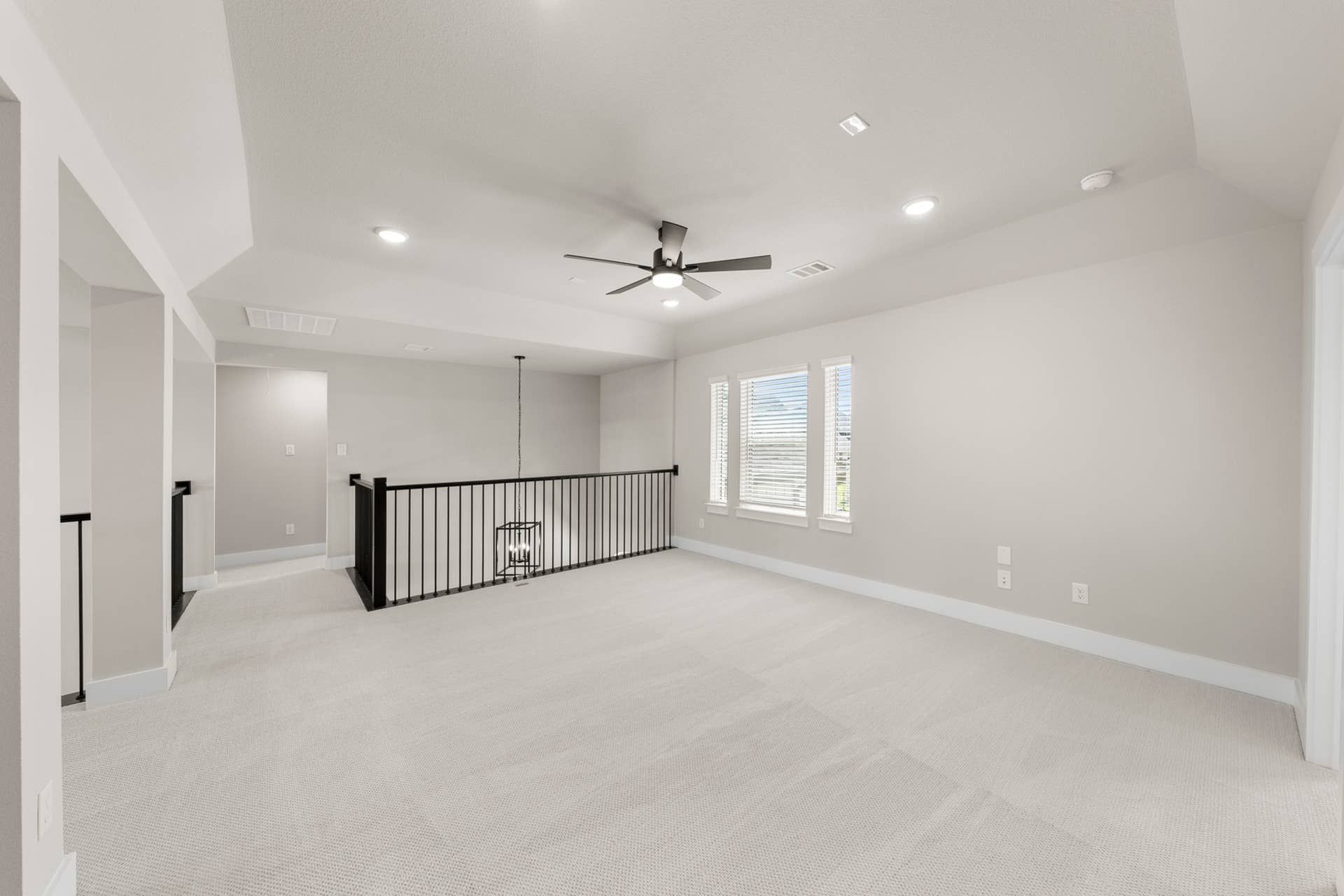 Spacious upper-level room with carpet, ceiling fan, and railing overlooking stairwell.