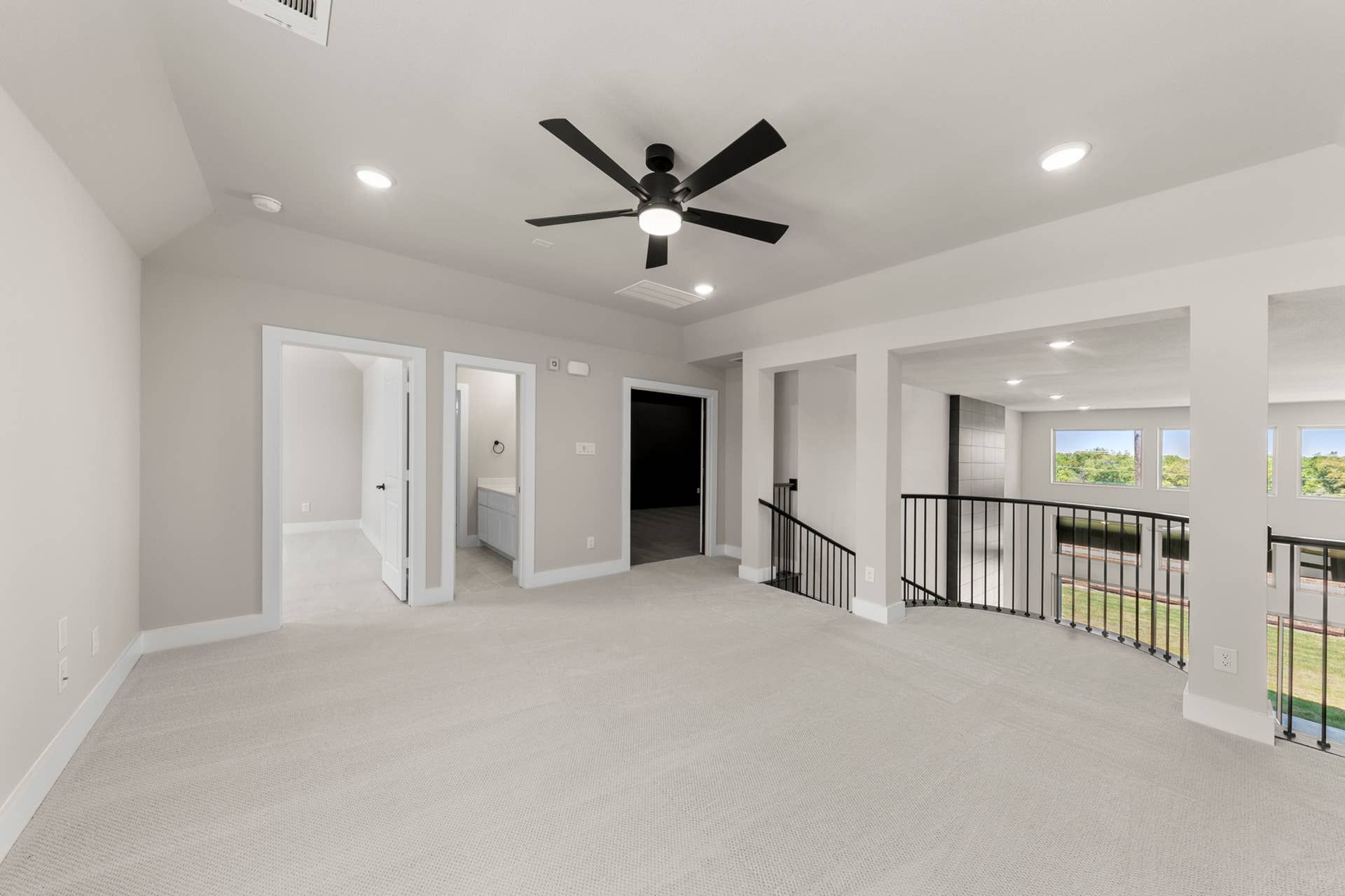 Spacious neutral-toned interior with ceiling fan and large windows overlooking greenery.