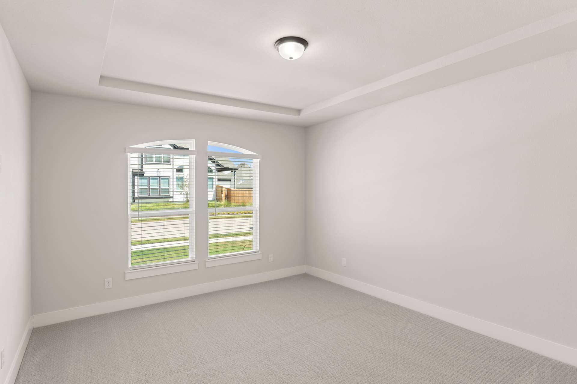 Bright empty room with arched window and tray ceiling.