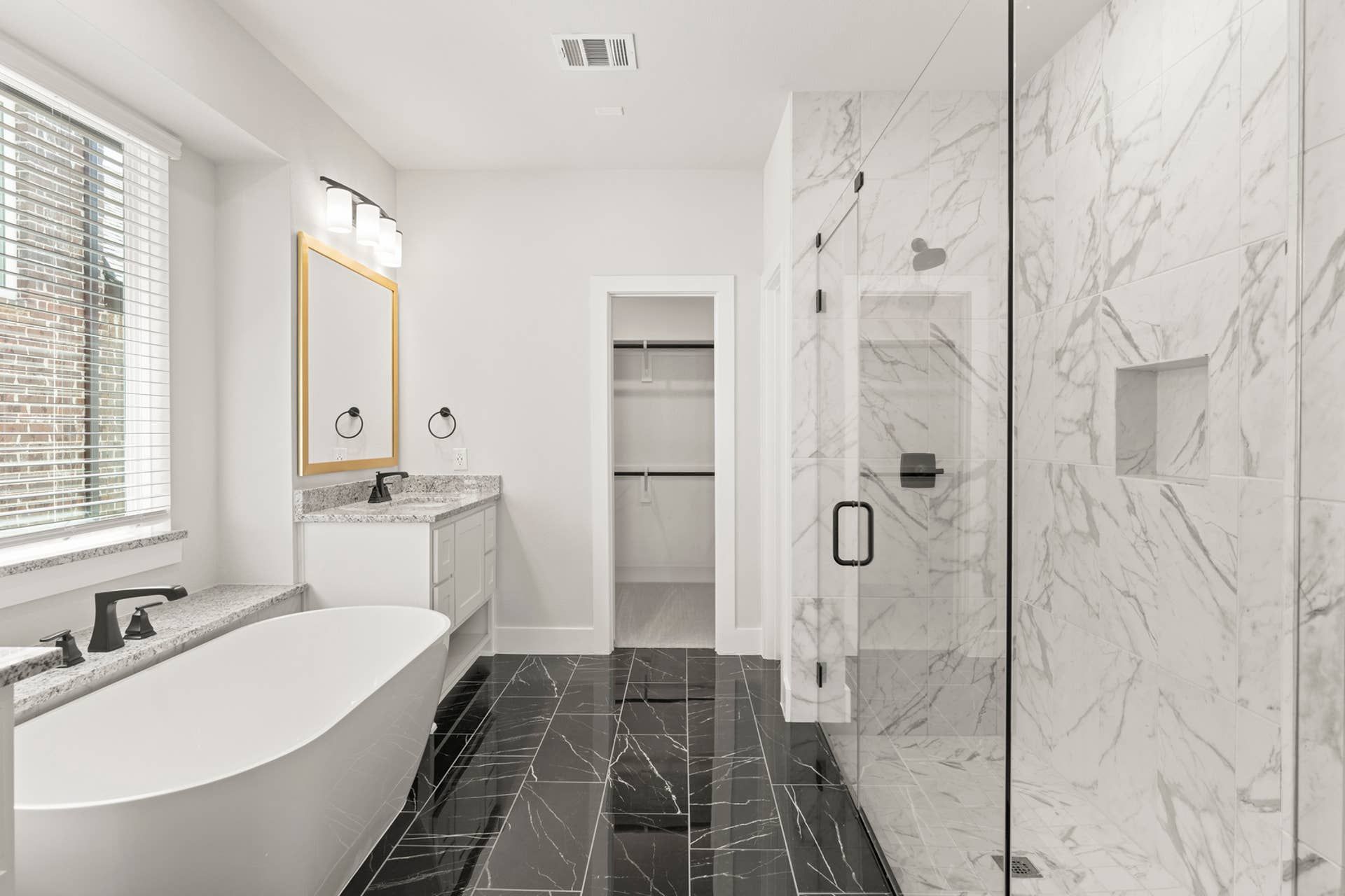 Luxurious bathroom with freestanding tub, marble shower, and sleek black floor tiles.