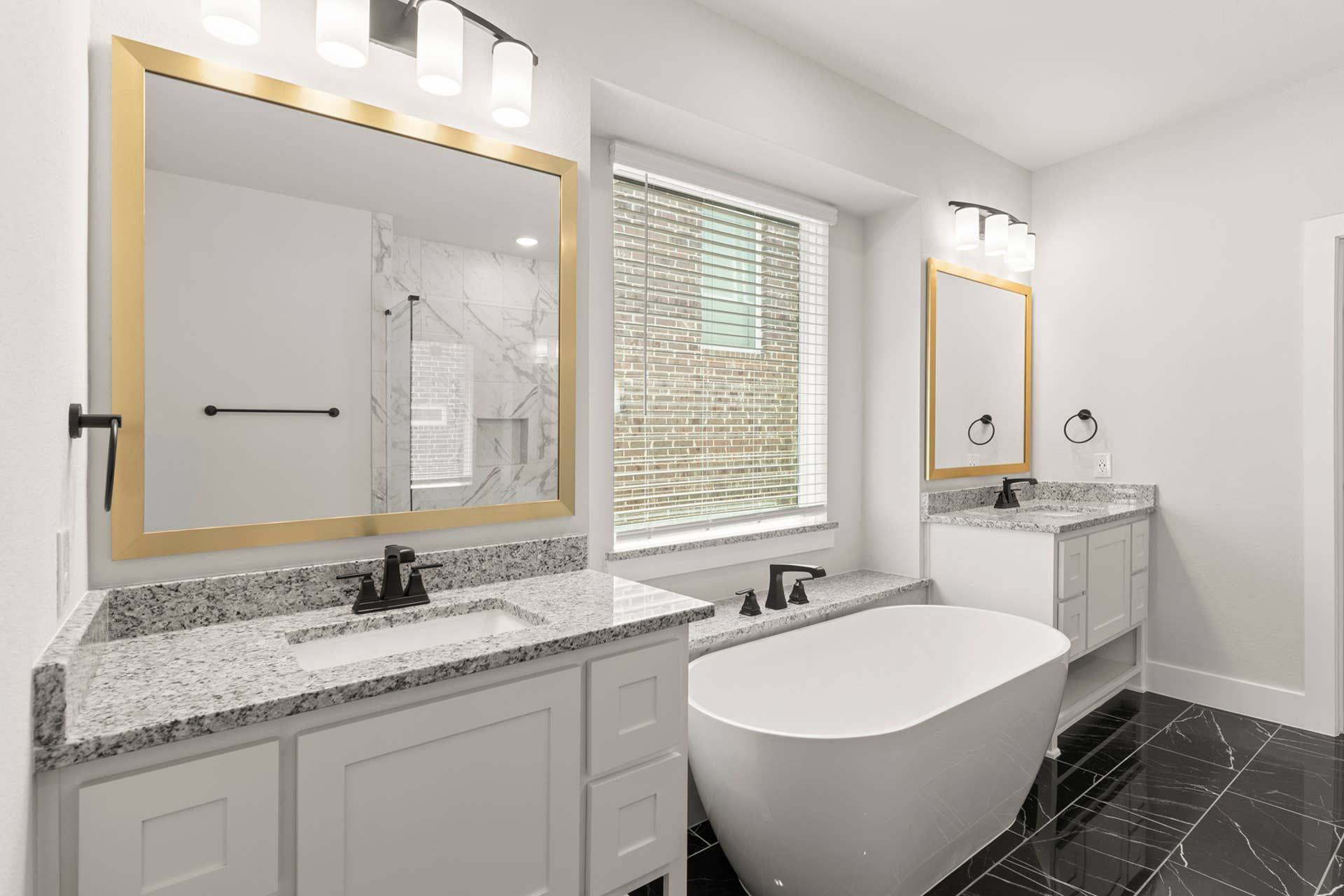Modern bathroom with freestanding tub, granite countertops, and large mirrors.