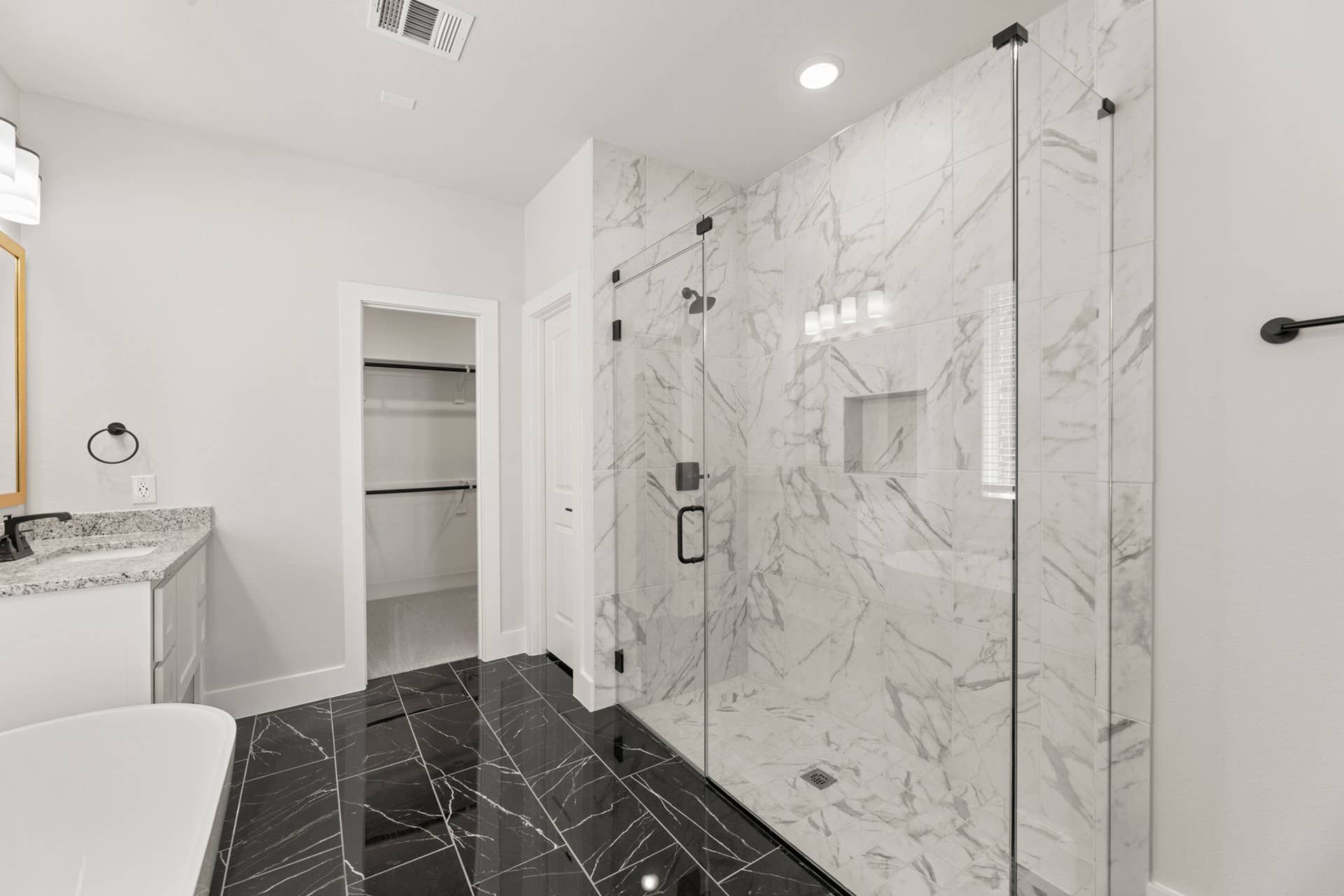 Luxurious bathroom with marble shower, black tile floor, and granite countertop.