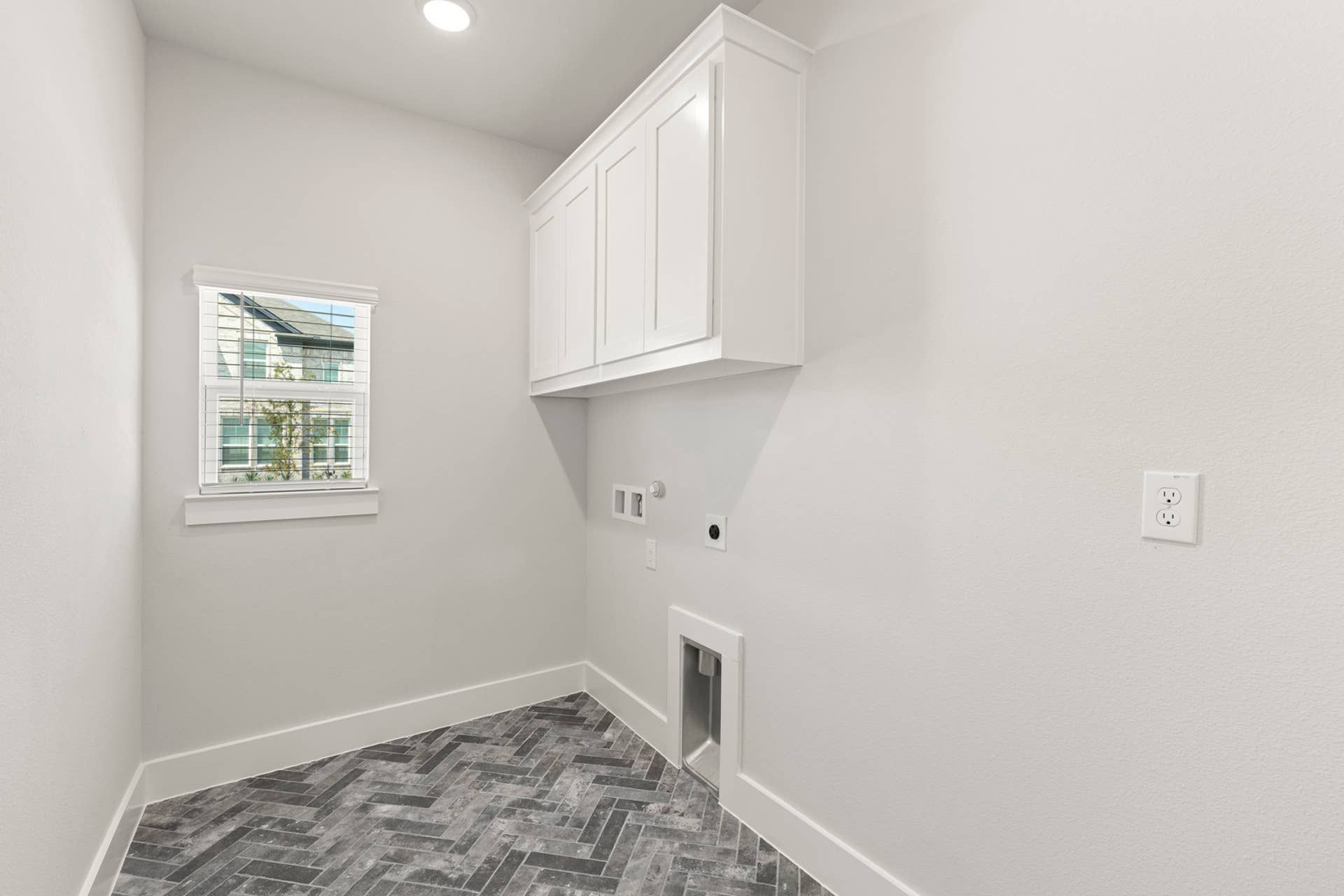 Modern utility room with herringbone tile floor and white cabinetry.