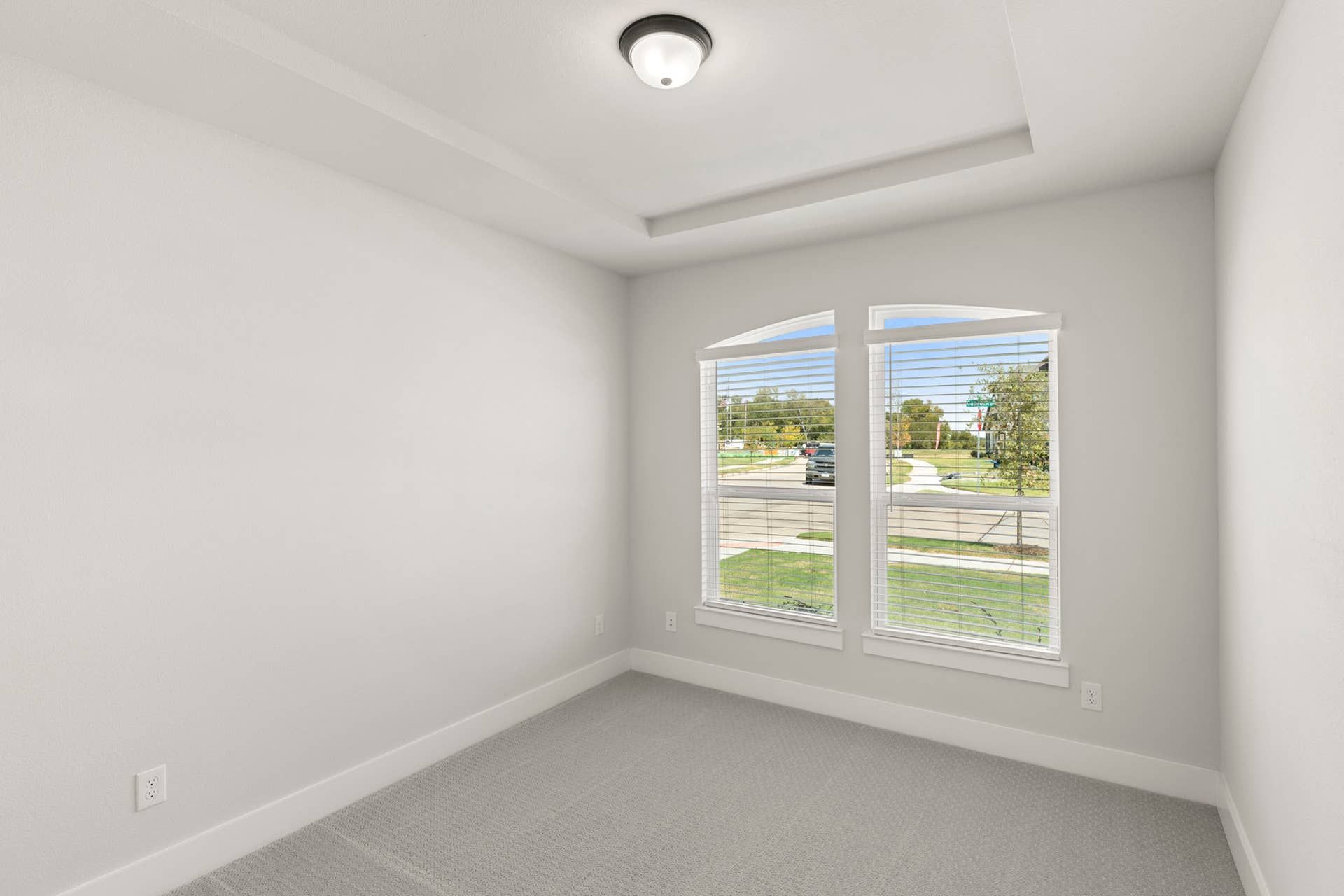 Bright bedroom with carpet flooring and large windows overlooking front yard.