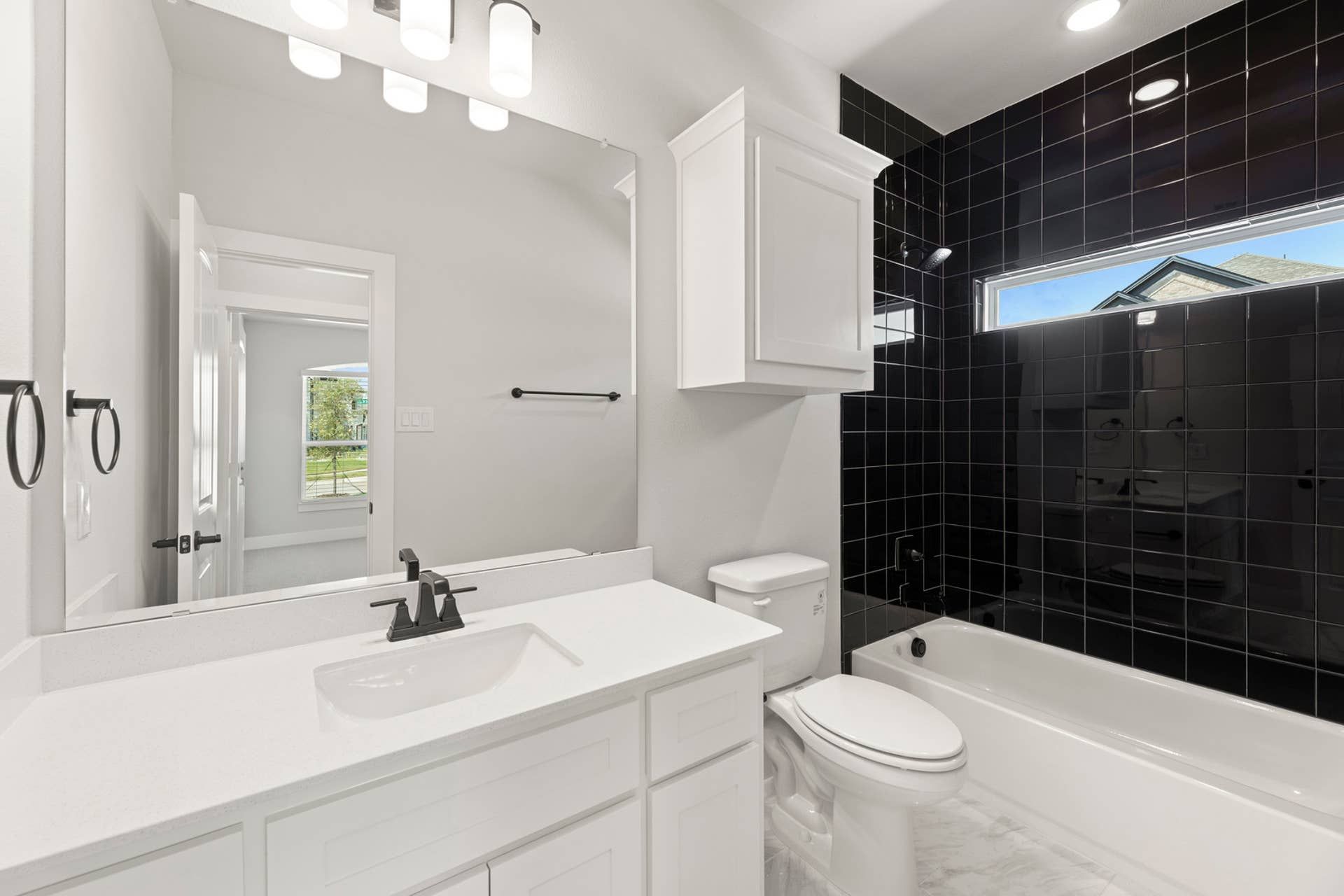 Modern bathroom with white vanity, black tiled shower, and natural light.