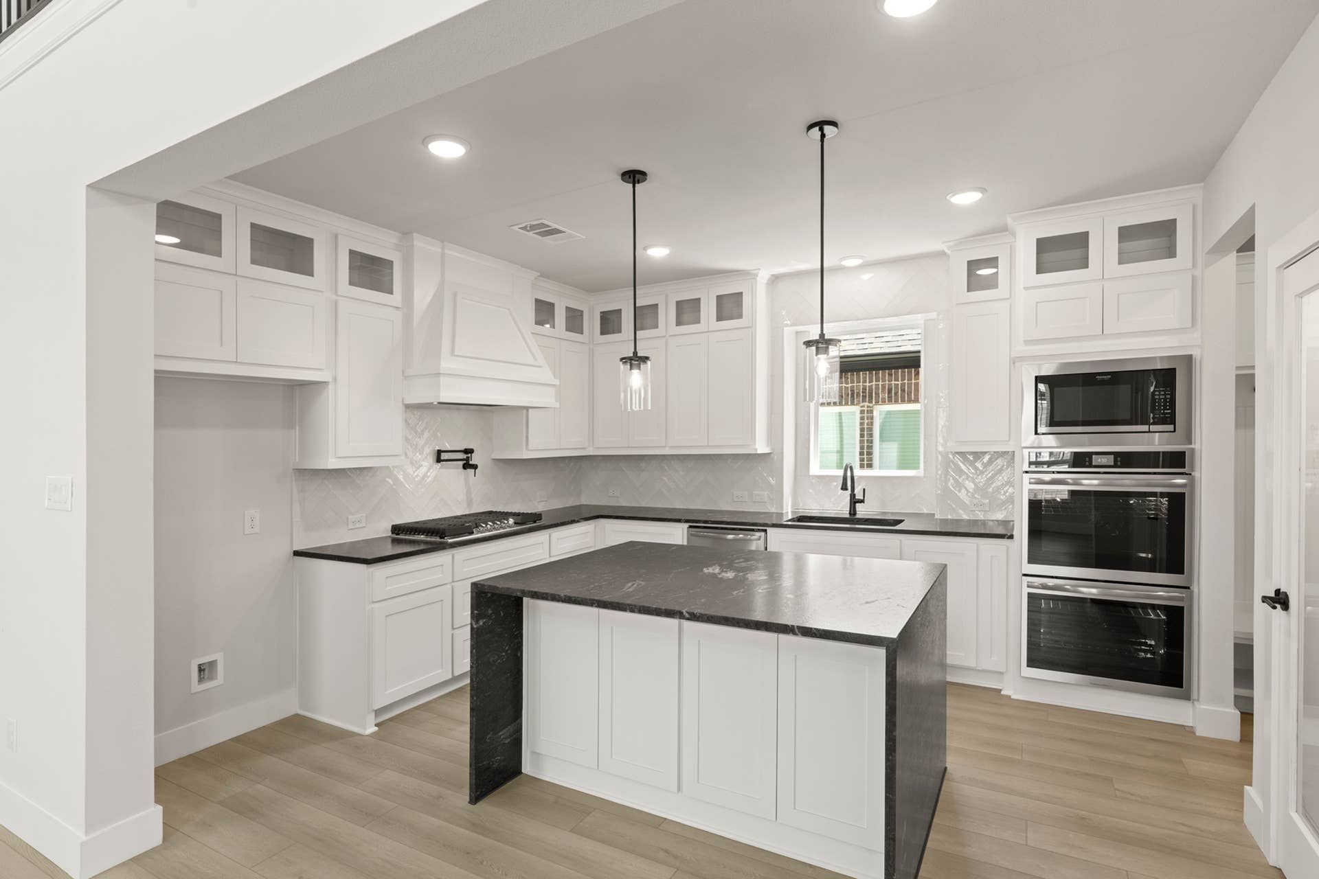 Modern kitchen with white cabinetry, black countertops, and island lighting fixtures.