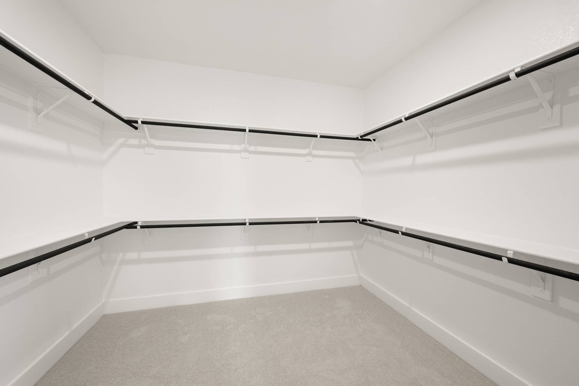 Spacious walk-in closet with white walls and black hanging rods.