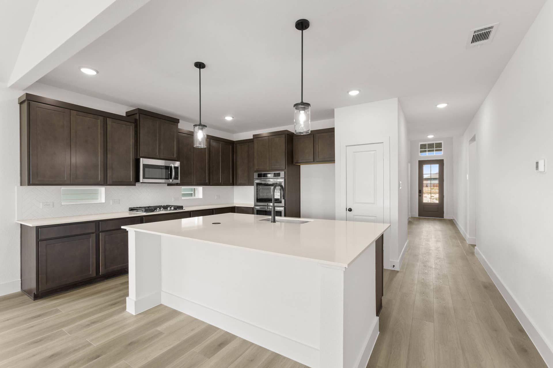 Modern kitchen with dark cabinets, white countertops, and pendant lighting.