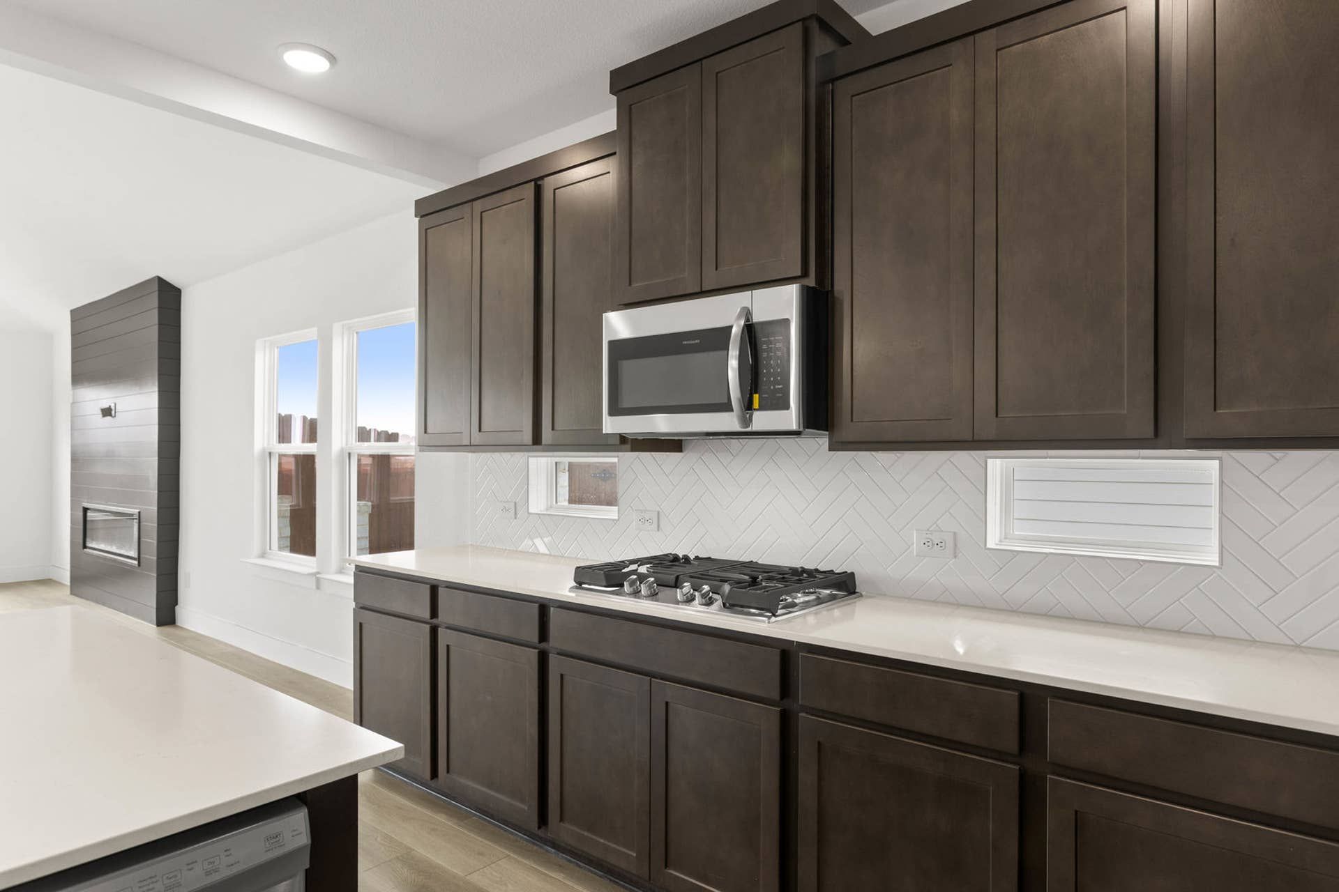 Modern kitchen with dark cabinets, gas stove, and white herringbone backsplash.