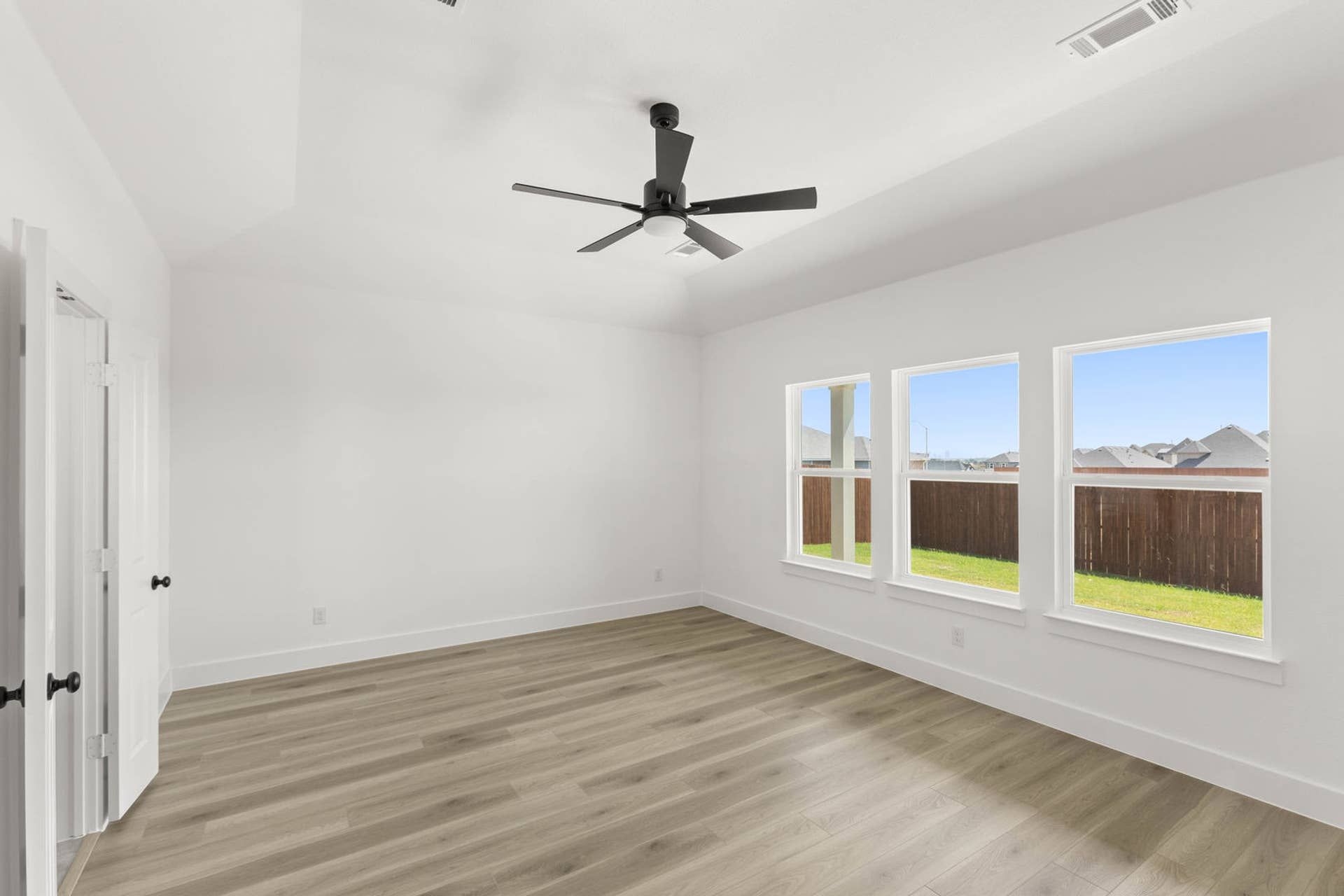 Spacious primary suite with large windows, wood flooring, and ceiling fan.