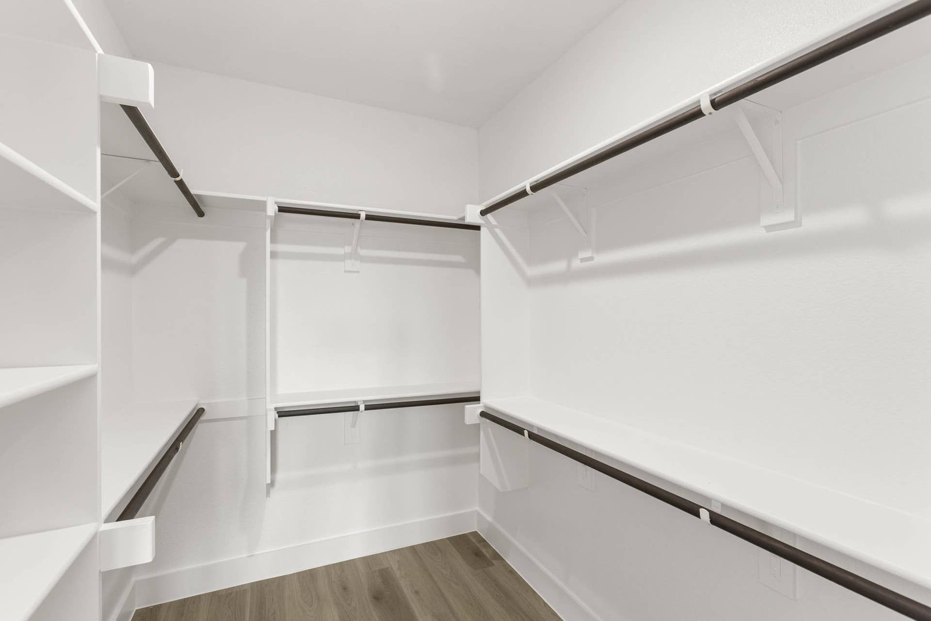Spacious walk-in closet with white shelving and dark wood rods.