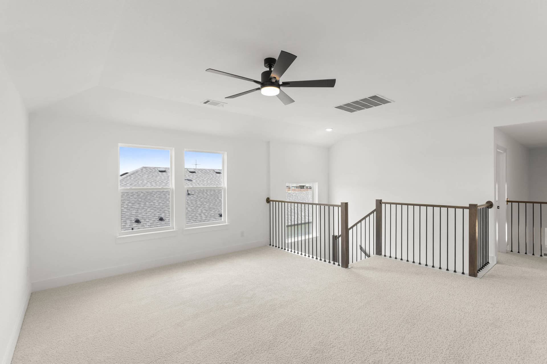 Spacious game room with ceiling fan and carpet flooring, featuring large windows.