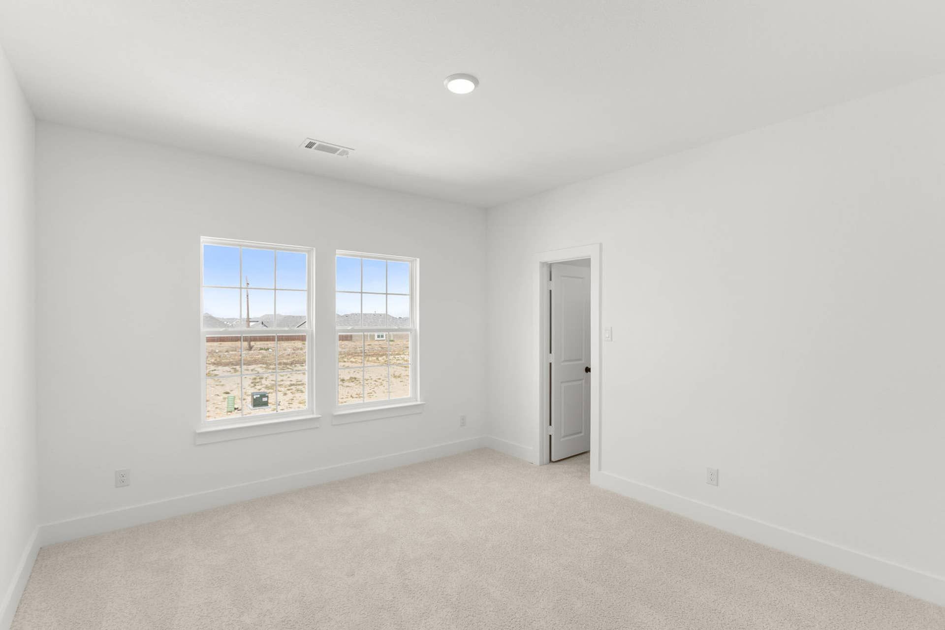 Bright bedroom interior with large windows and neutral carpet flooring.