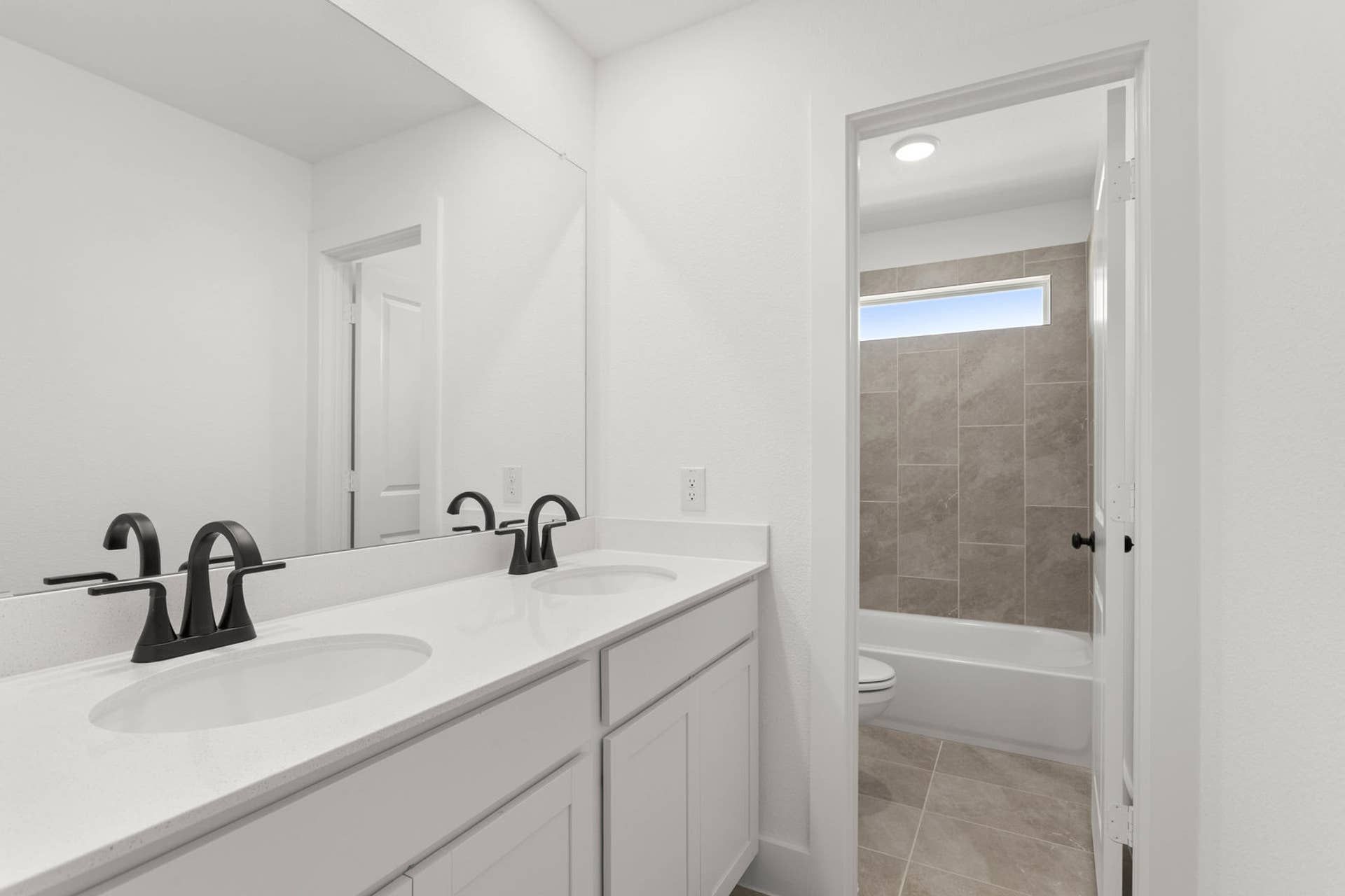 Modern bathroom with dual sinks, large mirror, and tiled shower area.
