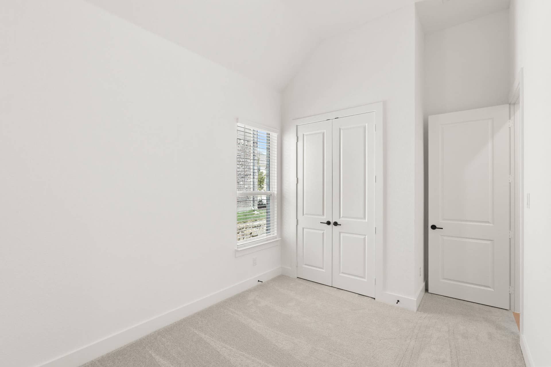Bright bedroom with carpet, closet doors, and a window with blinds.