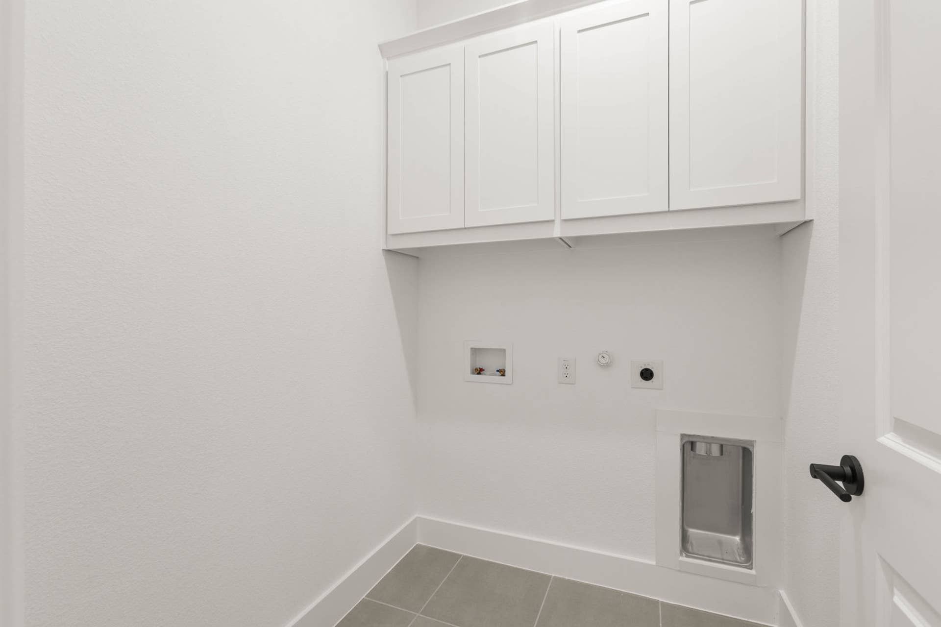 Modern utility room with white cabinets and laundry hookups.
