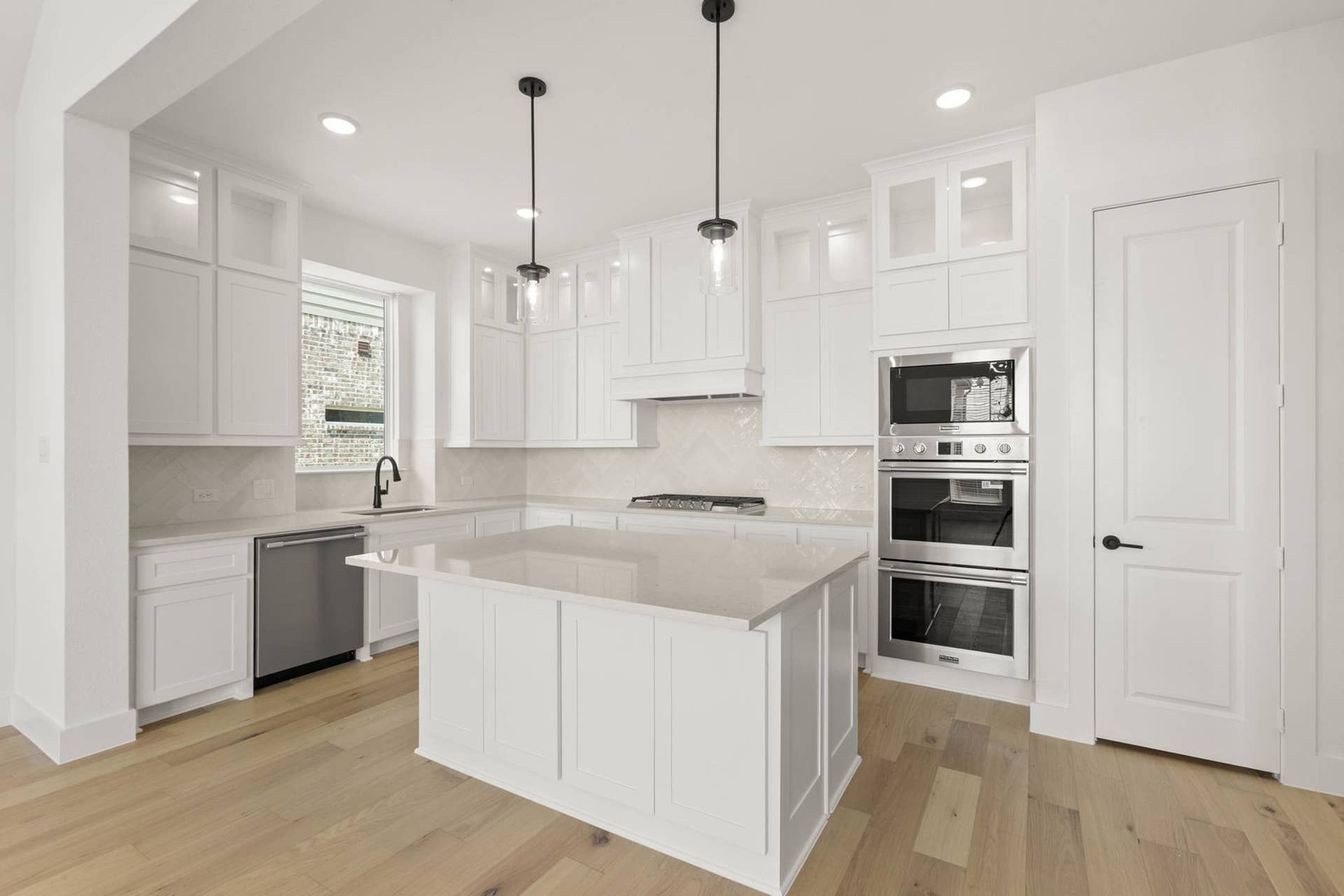 Modern kitchen with white cabinetry, island, stainless steel appliances, and pendant lighting.