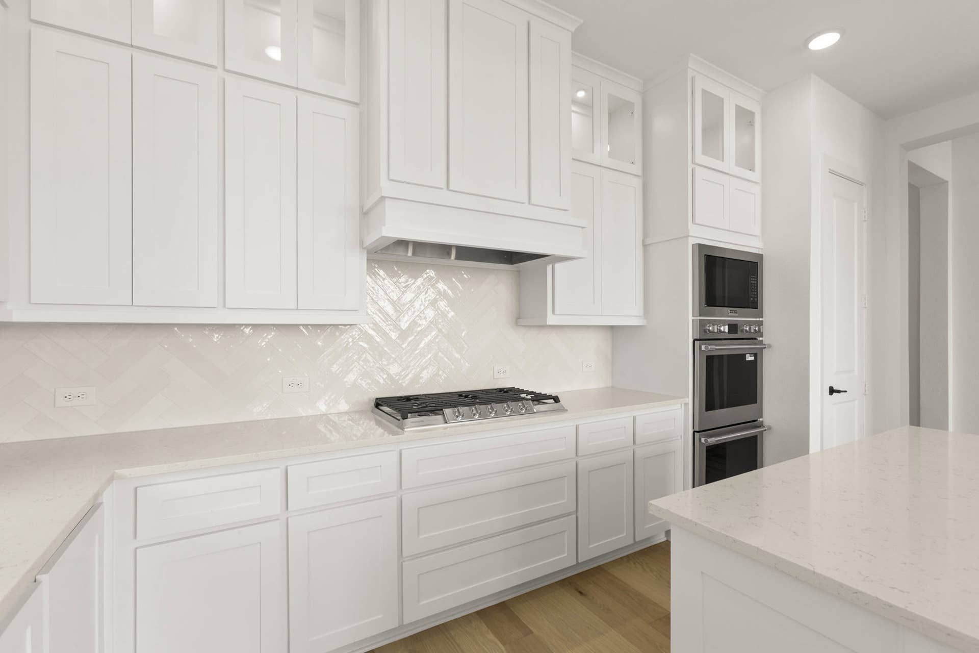Modern kitchen with white cabinetry, herringbone backsplash, and stainless steel appliances.