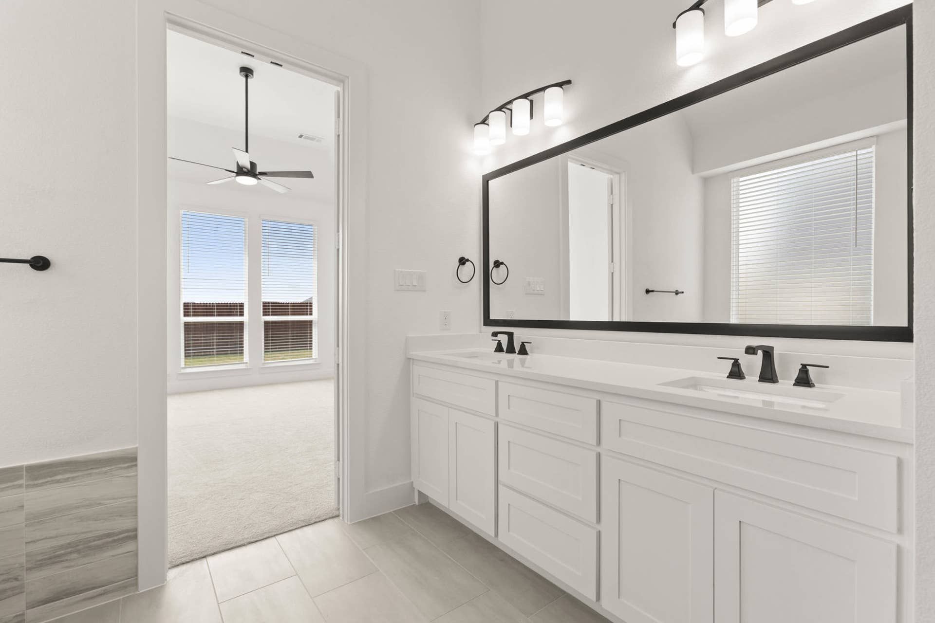 Modern bathroom with double vanity and large mirror, leading to a bright bedroom.