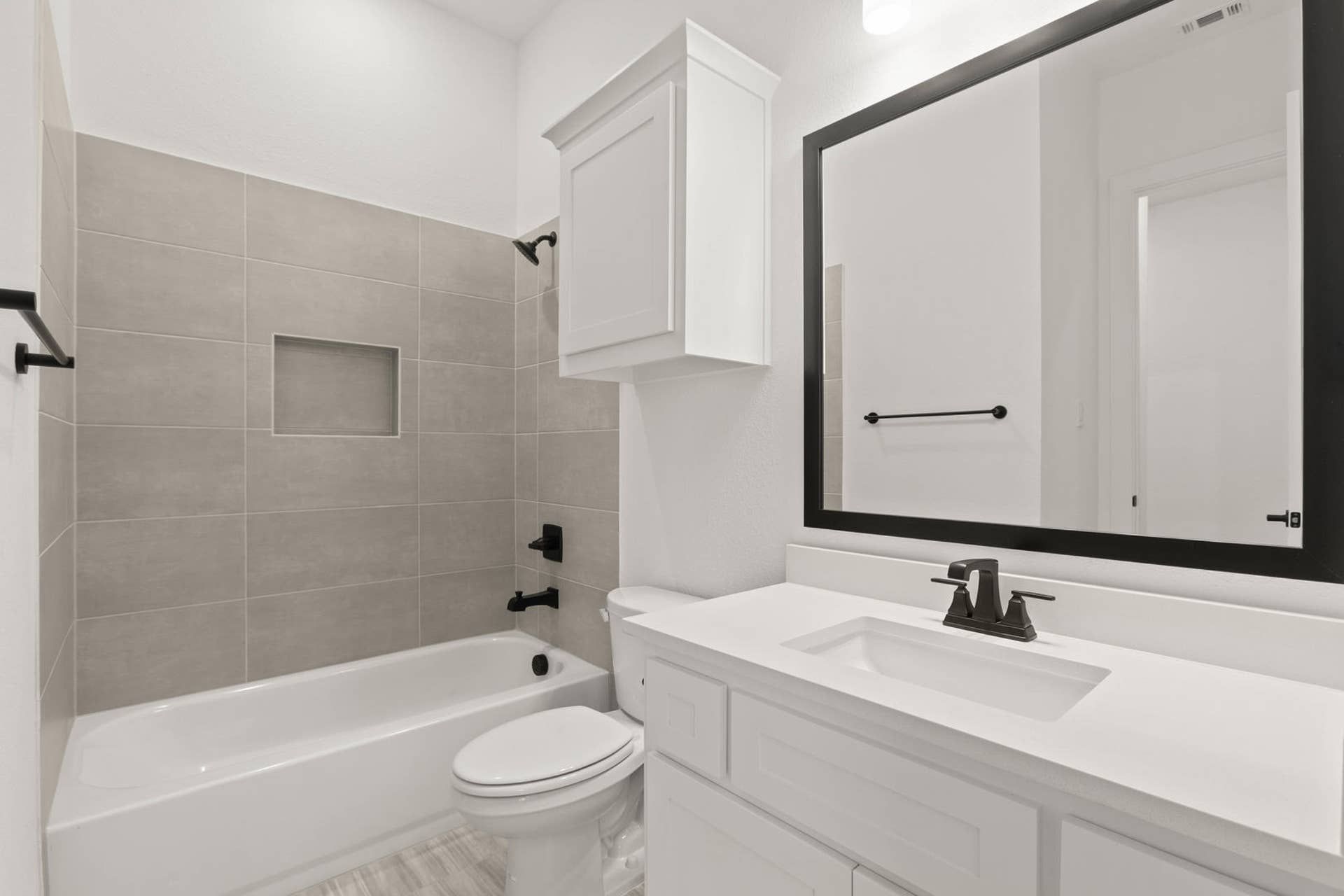 Modern bathroom with white cabinetry, large mirror, and tiled bathtub.