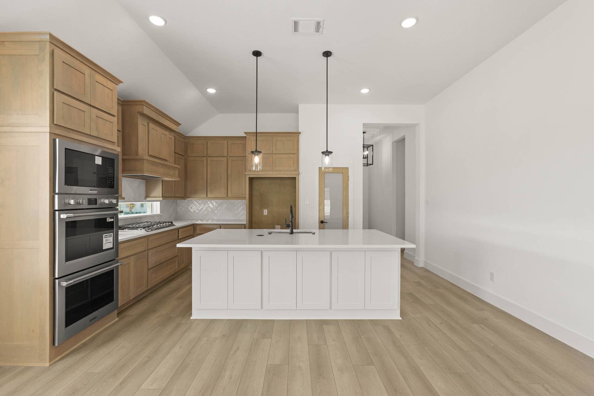 Modern kitchen with wood cabinetry, island, and stainless steel appliances.