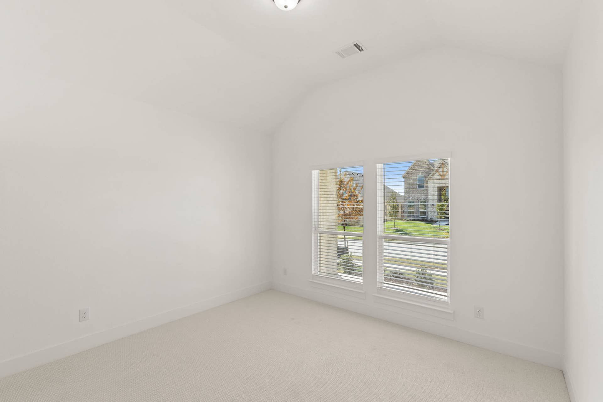 Bright, empty bedroom with large window and neutral carpet.