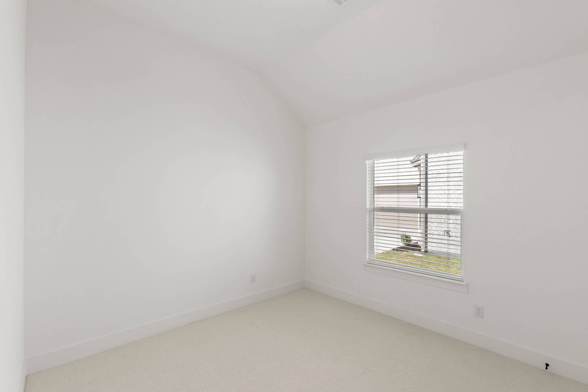 Minimalist bedroom with white walls and carpet, featuring a single window.