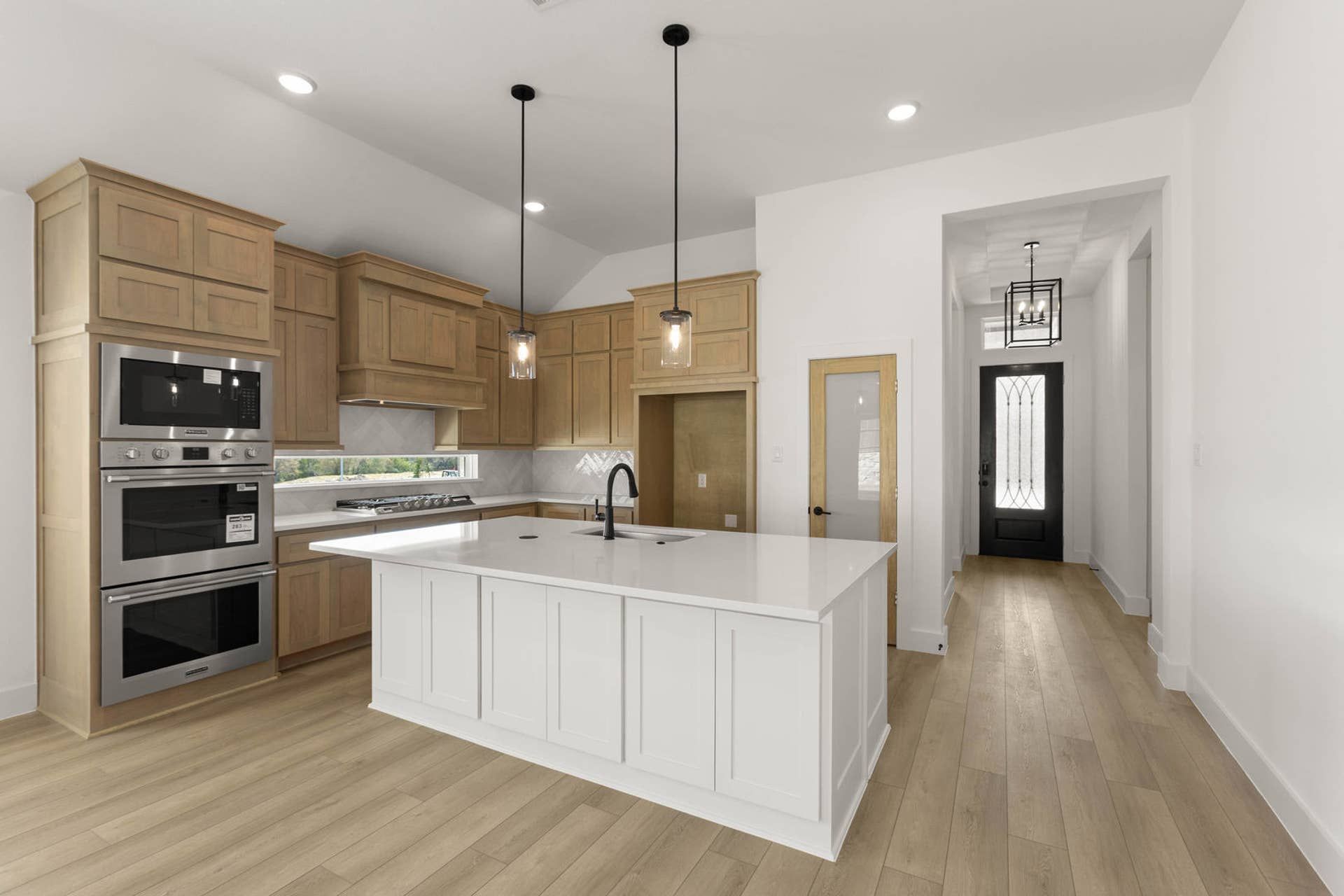 Modern kitchen with wood cabinetry, white island, and stainless steel appliances.