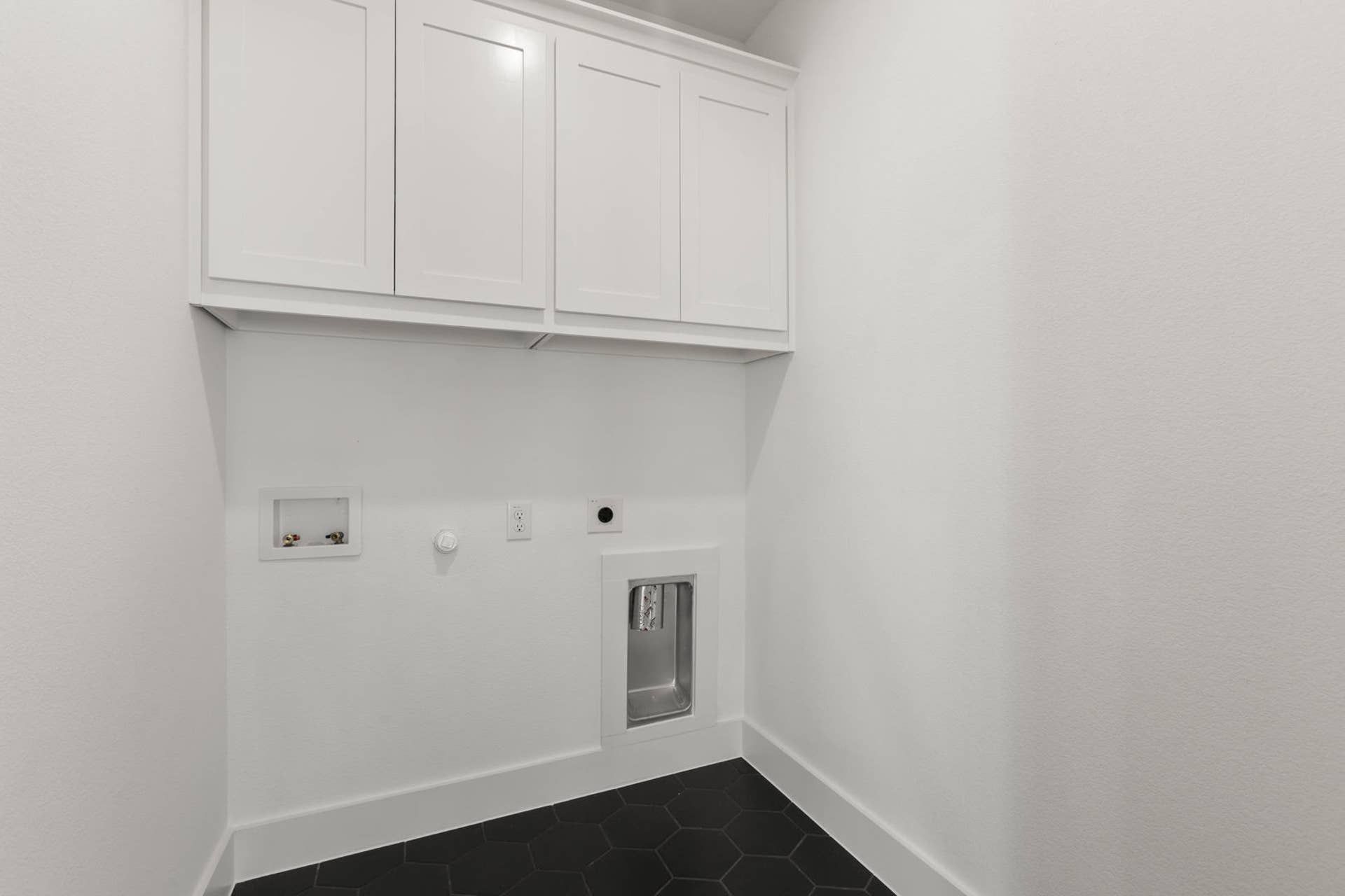 Modern utility room with white cabinets and black hexagonal floor tiles.