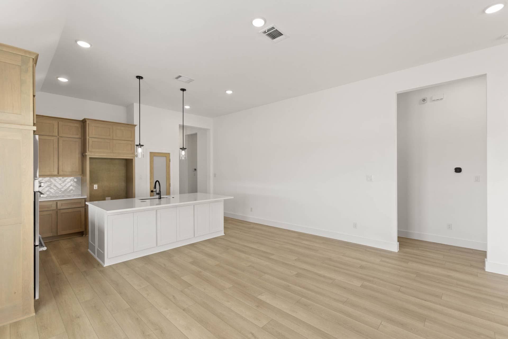 Spacious modern kitchen with island, pendant lighting, and light wood cabinetry.