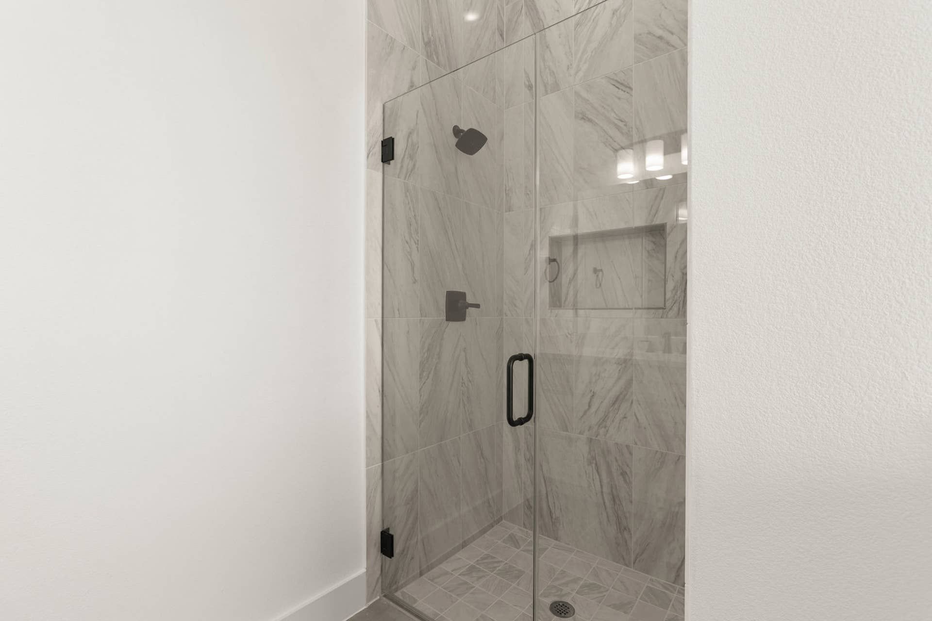 Modern glass-enclosed shower with marble tile in primary suite bathroom.