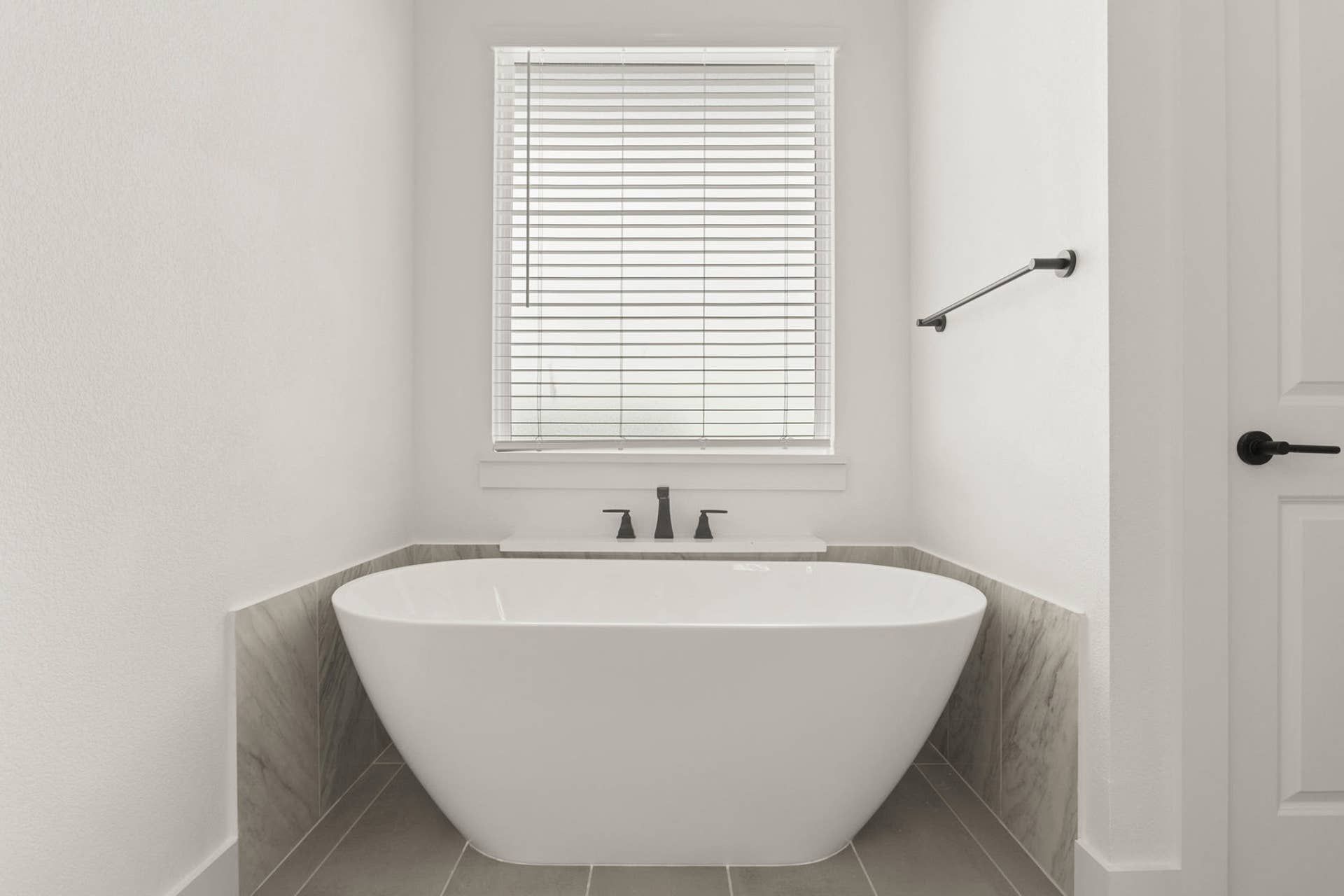 Minimalist bathroom with freestanding bathtub, modern faucet, and window blinds.
